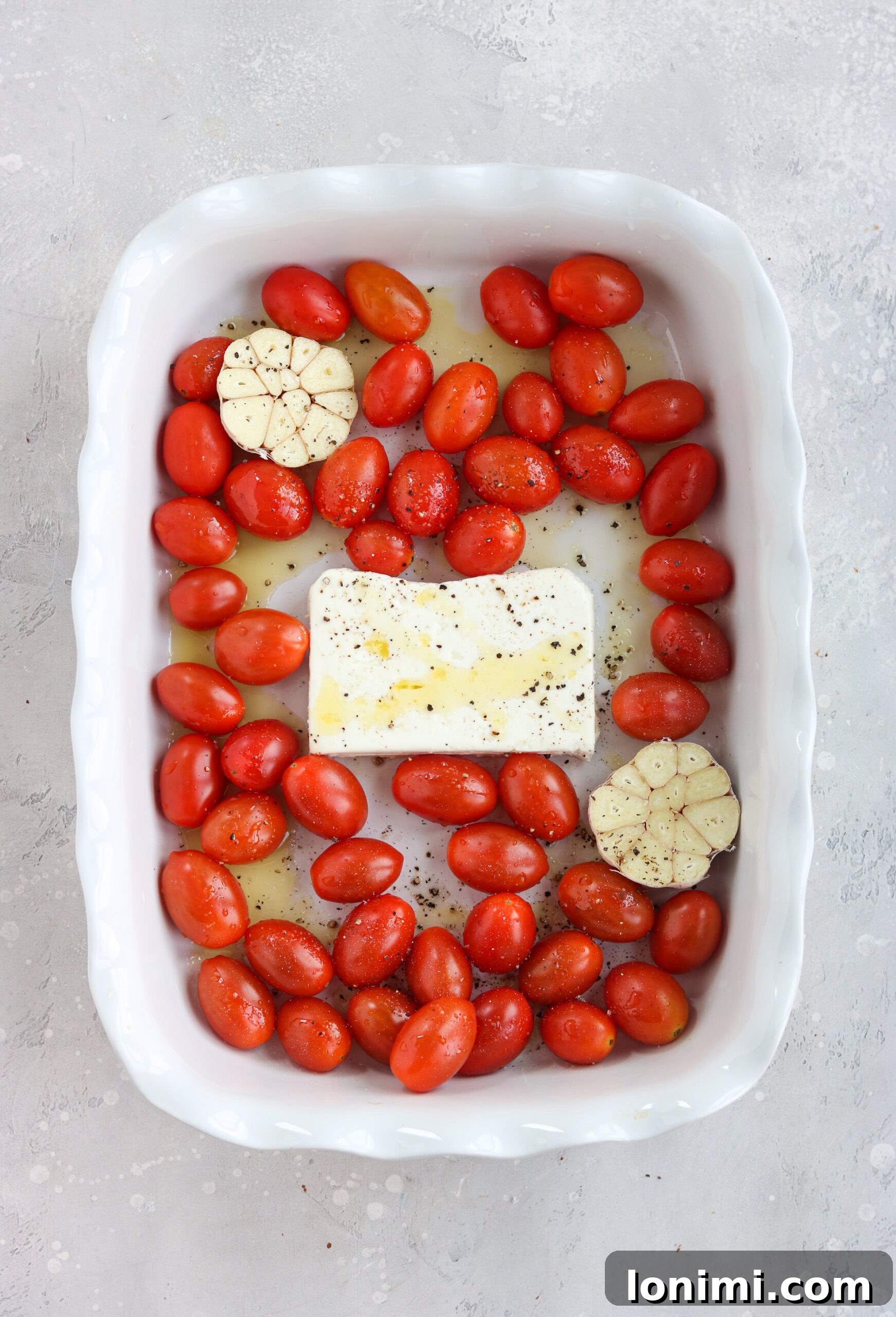 Cherry tomatoes and garlic in a casserole dish, ready for baking