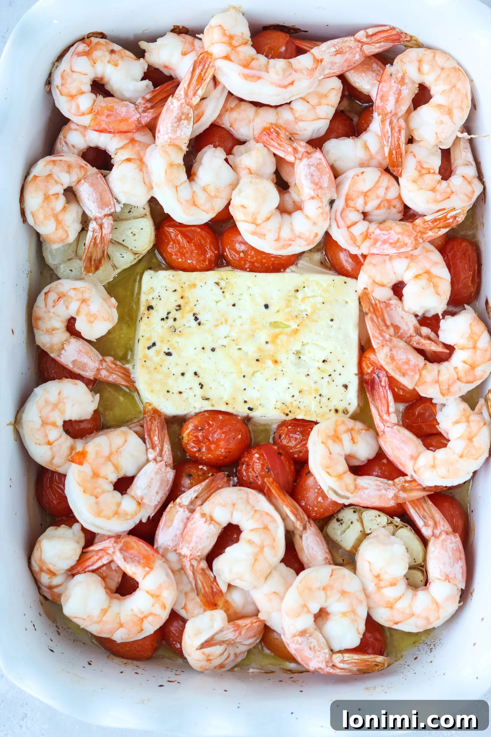 Assorted ingredients for baked feta pasta with shrimp, including feta, tomatoes, garlic, shrimp, and pasta