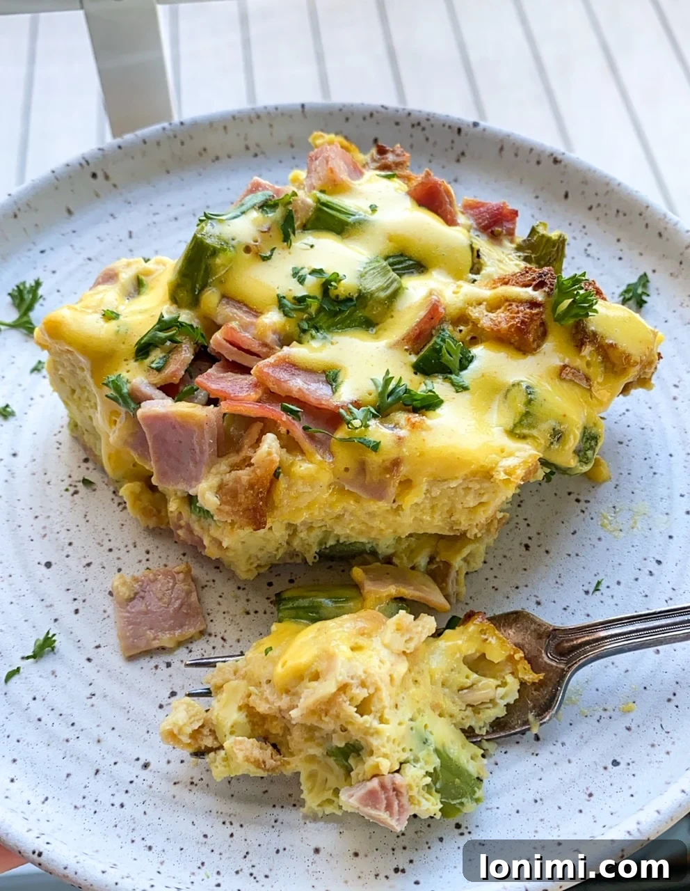 A beautifully plated slice of Gluten-Free Overnight Eggs Benedict Casserole with a fork, emphasizing its delightful texture and the vibrant topping.
