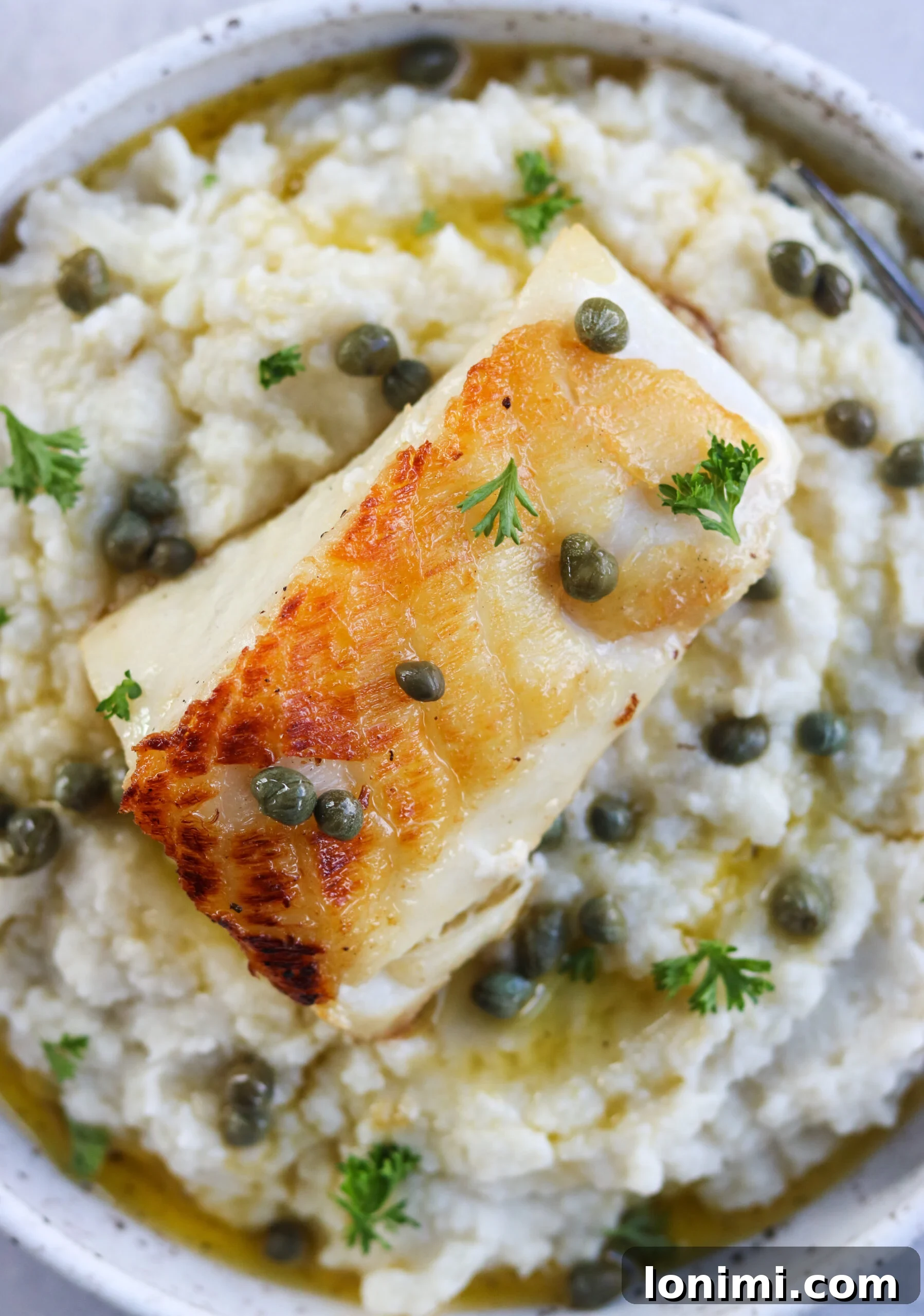 Closeup of pan-seared fish on top of creamy cauliflower mash, garnished with fresh herbs, showcasing a delicious low-carb serving idea.