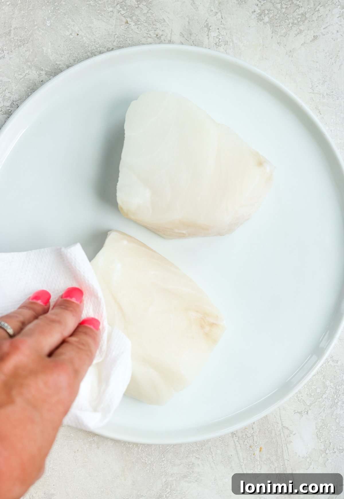 Blotting excess moisture from a sea bass fillet with paper towels, a crucial step for crispy skin.