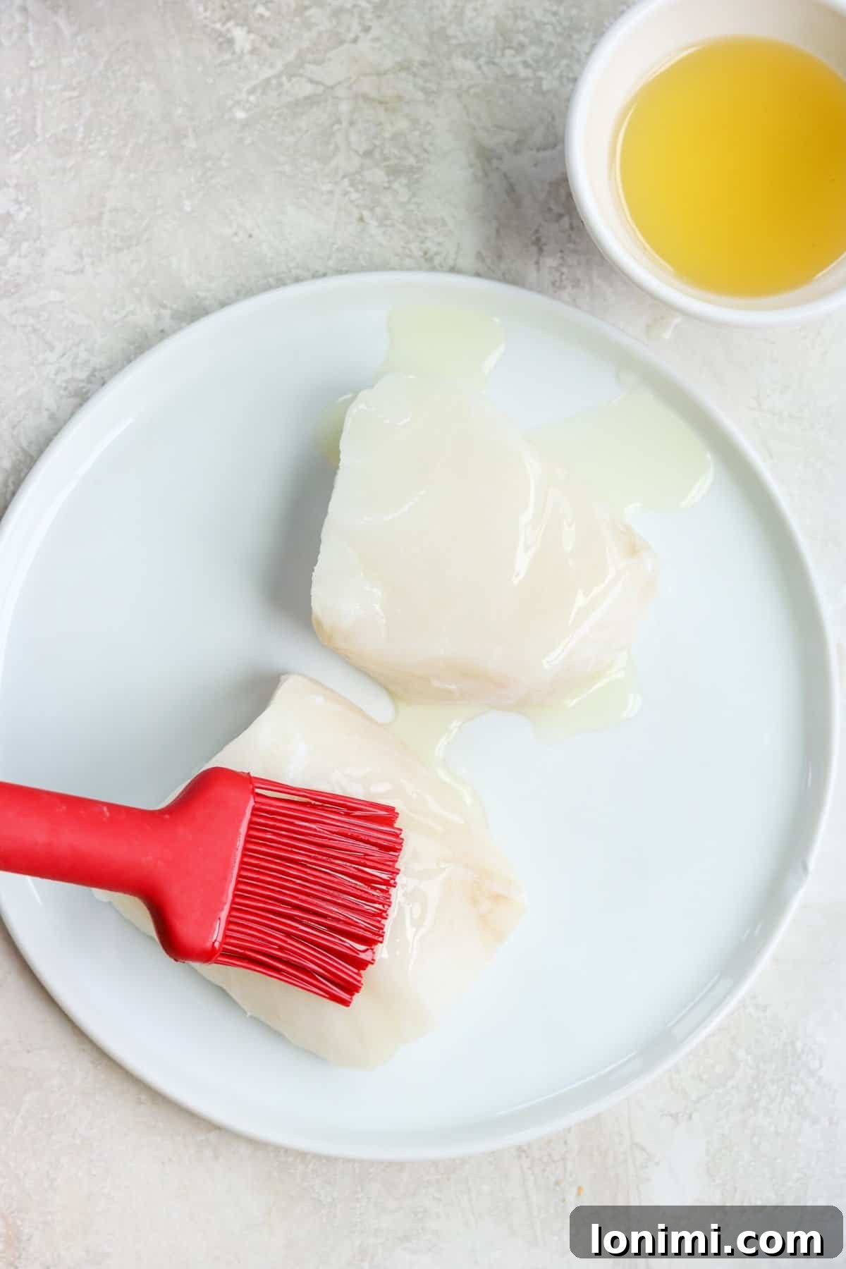 A red brush applying oil onto sea bass fillets, preparing them for seasoning.