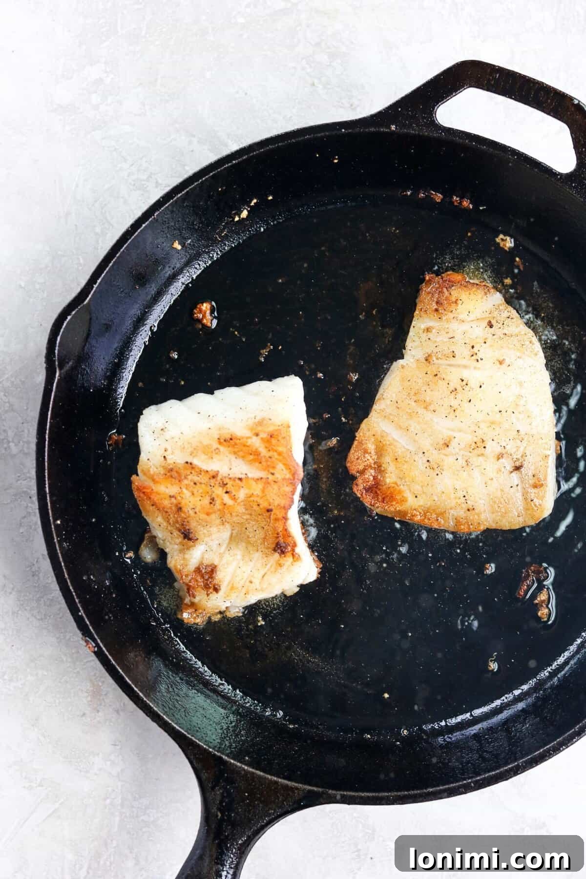 Perfectly pan-seared Chilean sea bass, golden brown and ready for the oven, resting in a cast iron pan.
