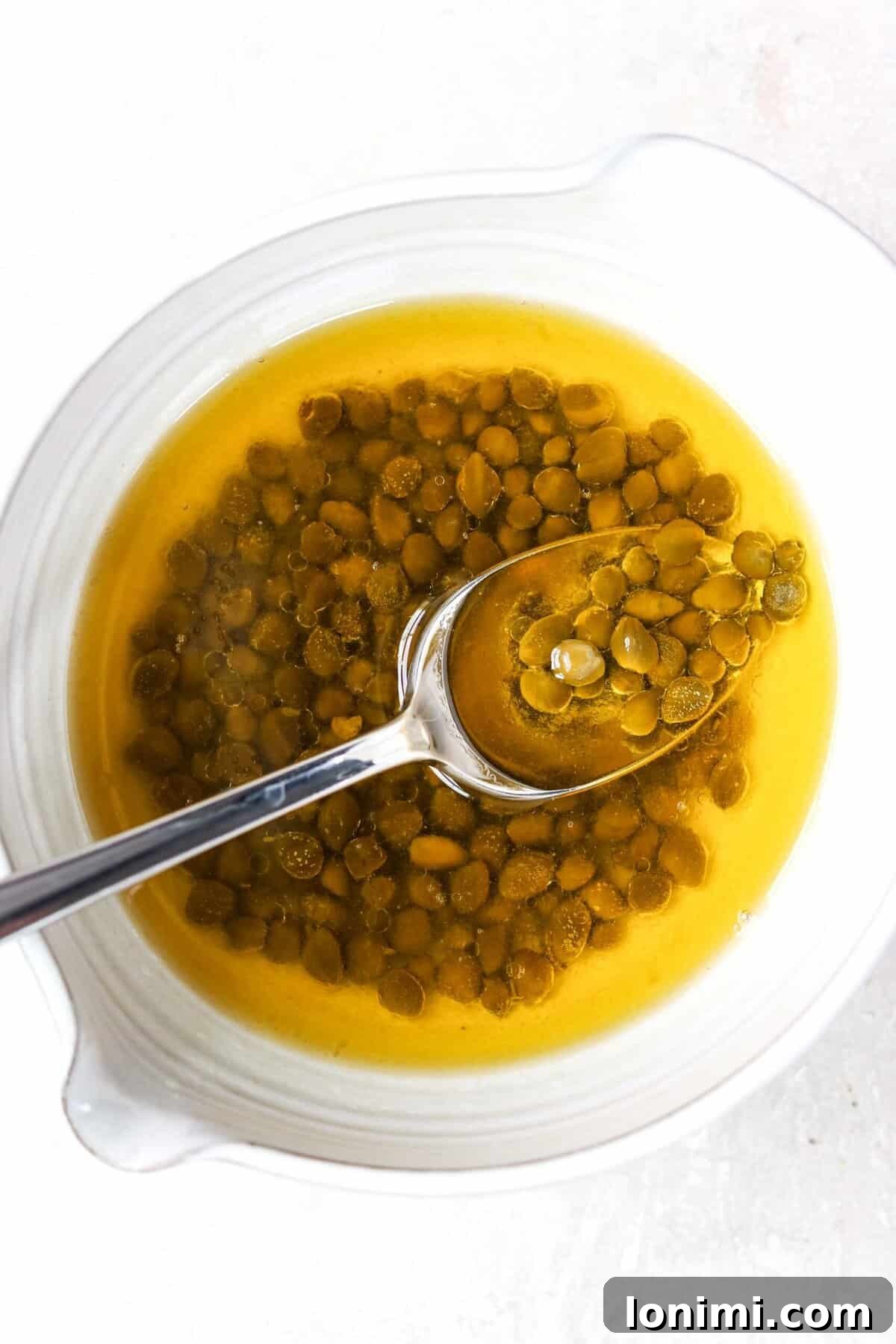 A small white bowl filled with melted butter and briny capers, ready to be combined with lemon juice.