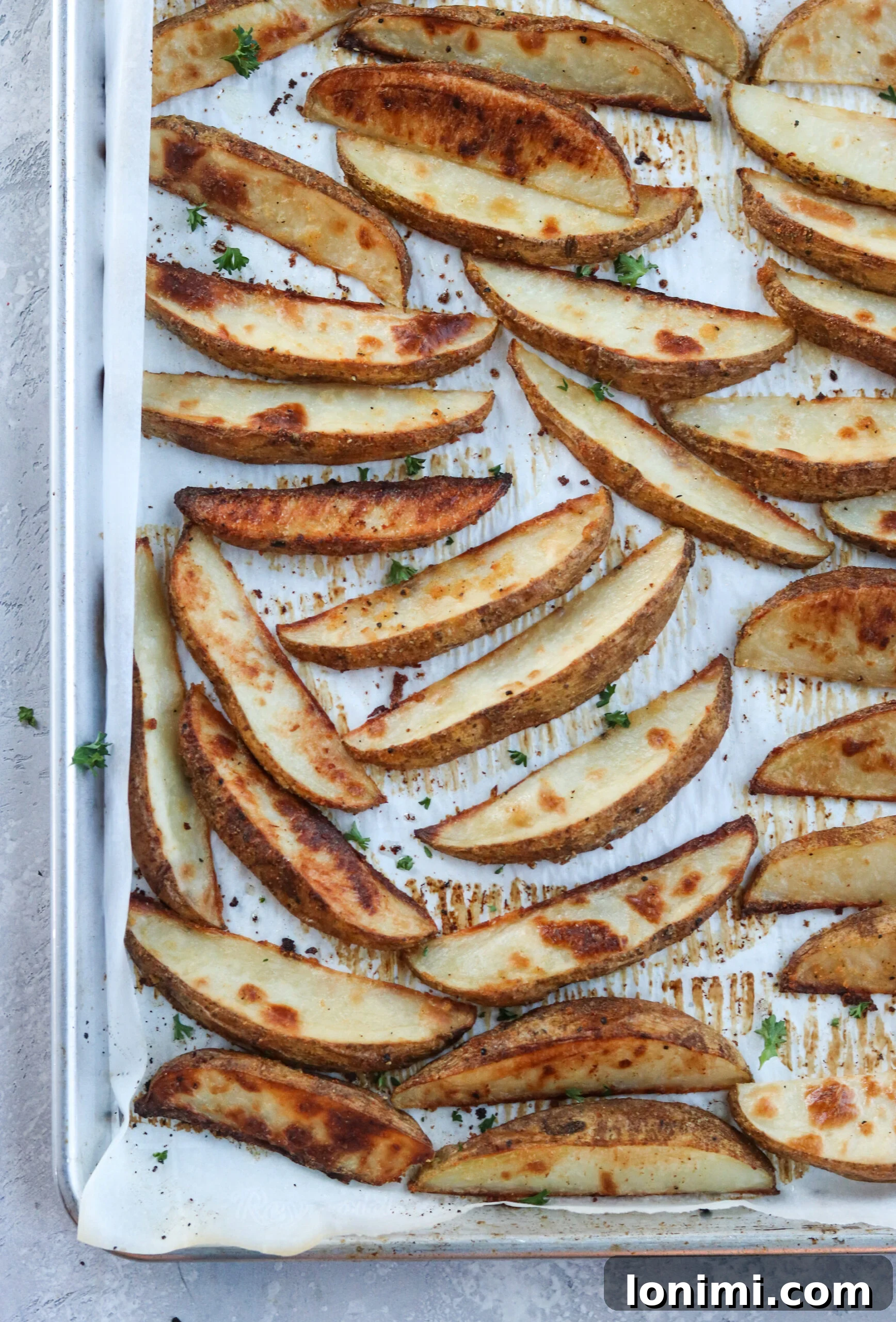 Golden brown crispy baked potato wedges spread on a baking sheet, fresh from the oven, ready to be served.