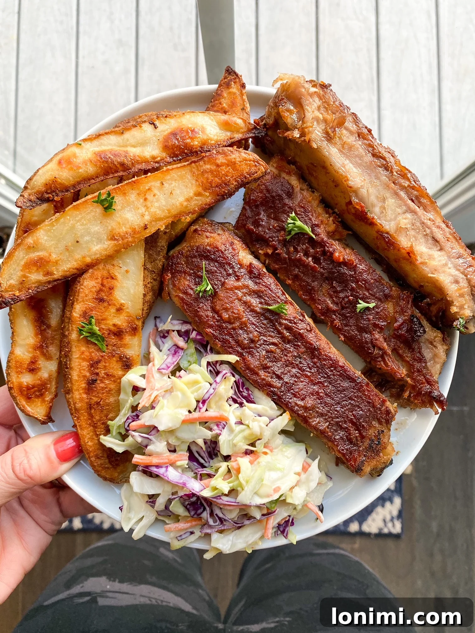 Perfectly cooked potato wedges and ribs served on a white plate with green garnish.