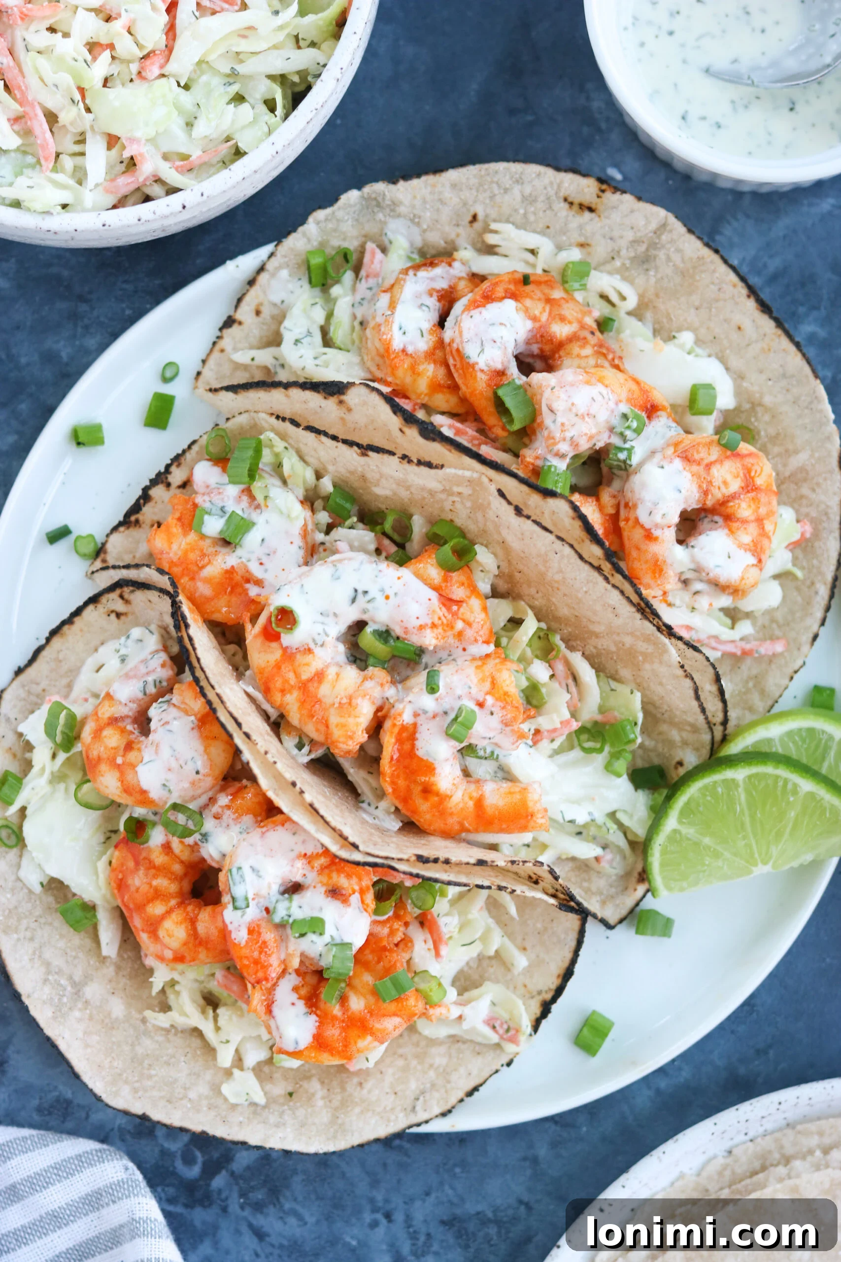 Delicious Paleo Buffalo Shrimp Tacos with fresh lemon A trio of vibrant Paleo Buffalo Shrimp Tacos presented on a pristine white plate, garnished with a fresh lemon wedge, highlighting their appetizing appearance.