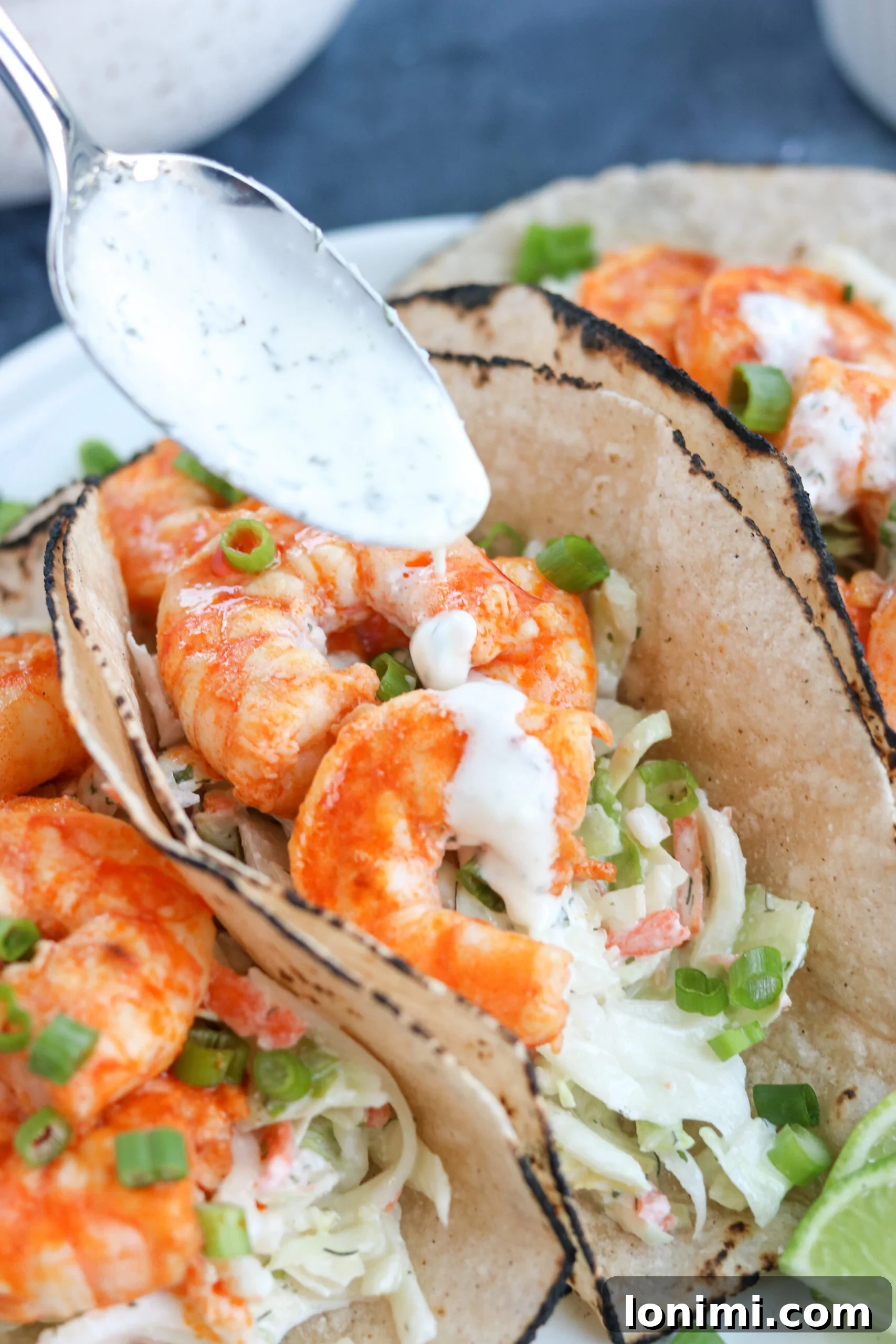 Adding sauce to shrimp taco A close-up shot of a hand gracefully drizzling creamy lime ranch sauce over a freshly assembled Paleo Buffalo Shrimp Taco, emphasizing the rich textures and flavors.