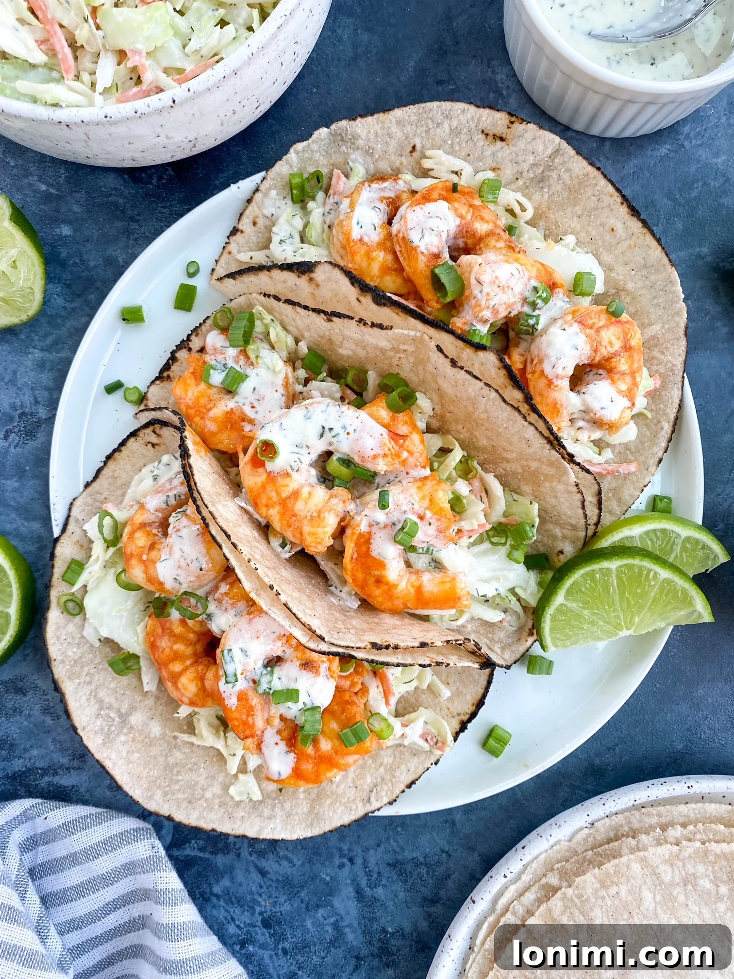 Beautifully presented shrimp tacos Four delicious looking Paleo Buffalo Shrimp Tacos arranged beautifully on a rustic white plate, garnished with fresh cilantro and lime wedges.