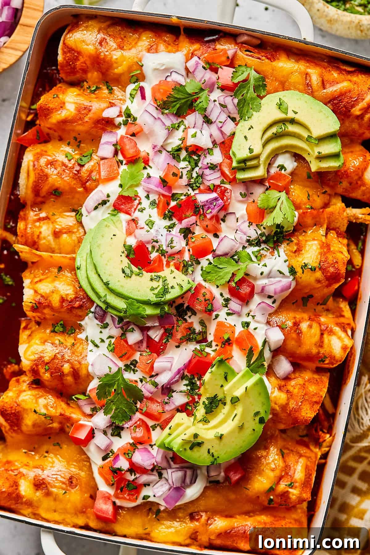 Weeknight Chicken and Black Bean Enchiladas 2 A vibrant casserole dish filled with baked chicken and black bean enchiladas, generously topped with fresh cilantro, sliced avocado, and a dollop of sour cream.