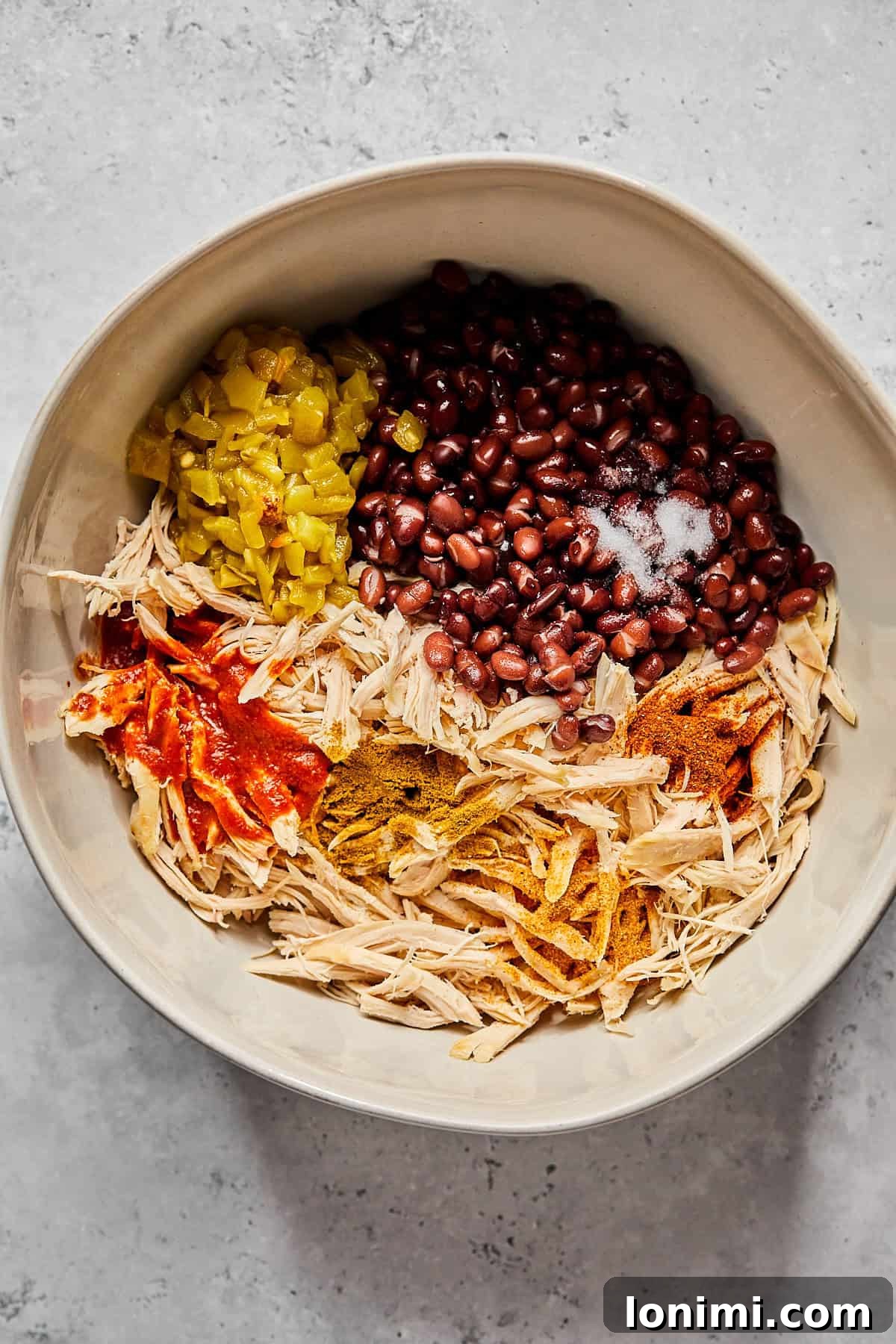 Weeknight Chicken and Black Bean Enchiladas 4 A large mixing bowl containing a savory blend of pulled rotisserie chicken, black beans, diced green chiles, and a vibrant array of Tex-Mex spices.
