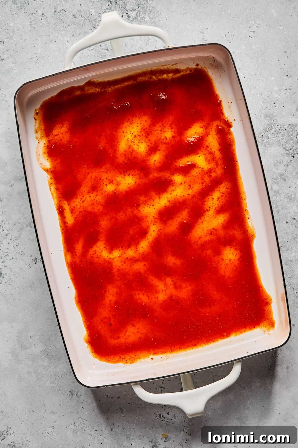 Weeknight Chicken and Black Bean Enchiladas 5 A 9x13 inch casserole dish with a thin, even layer of rich red enchilada sauce spread across its bottom.
