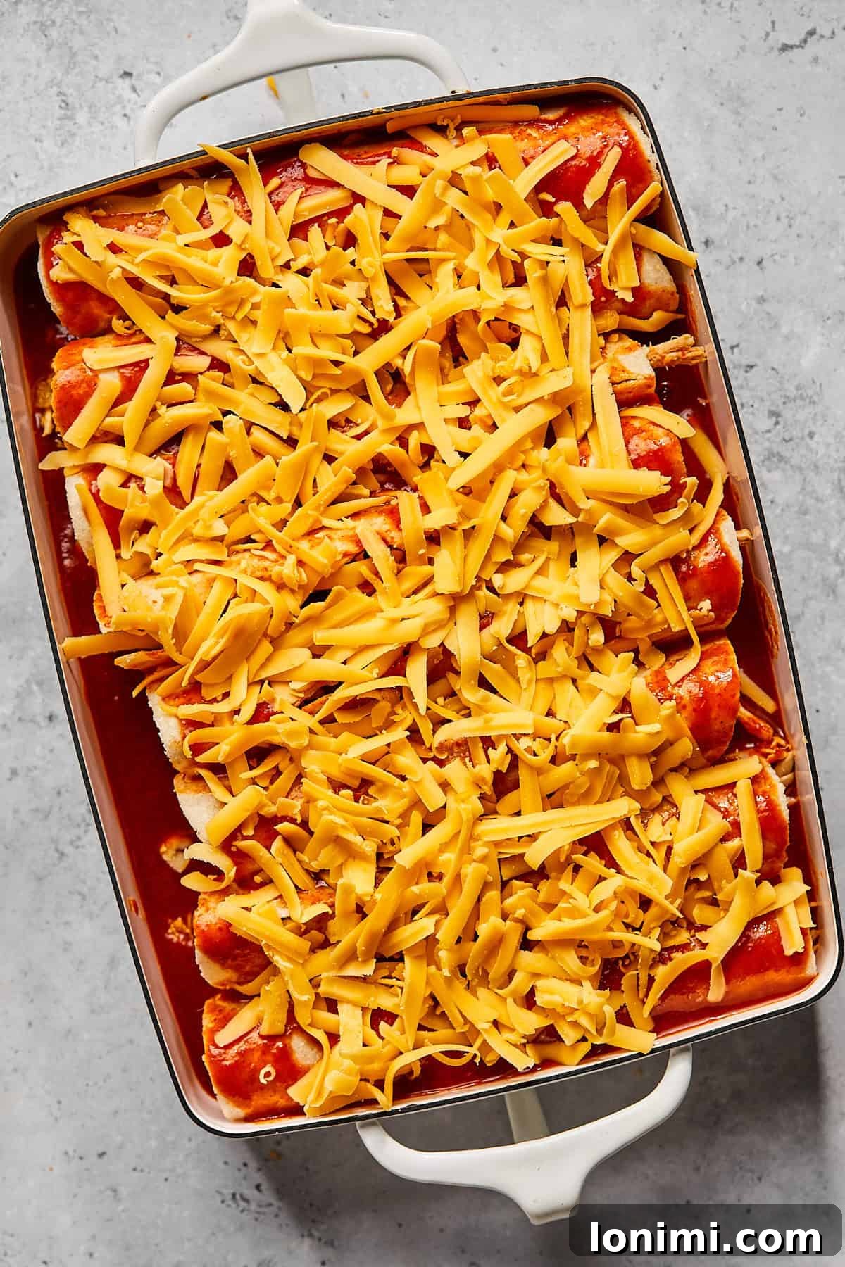 Weeknight Chicken and Black Bean Enchiladas 7 A casserole dish filled with perfectly rolled enchiladas, drenched in rich red enchilada sauce and topped with a generous layer of shredded cheddar cheese, ready for baking.