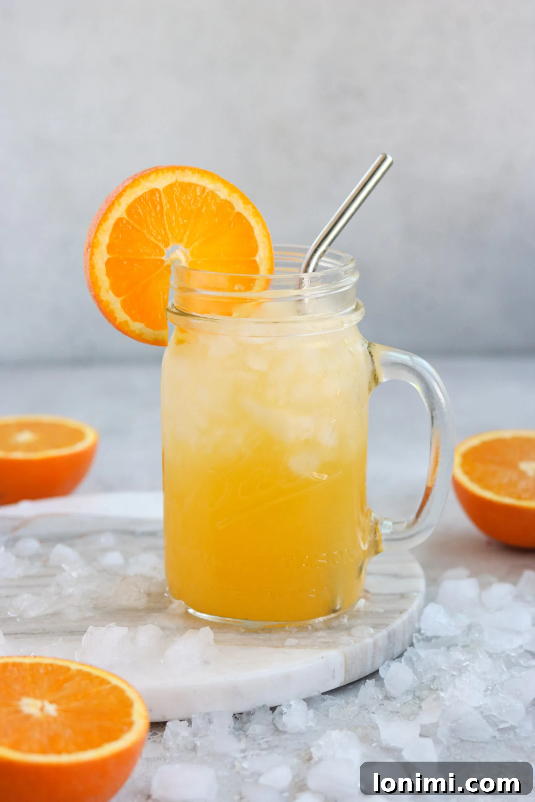 A vibrant Gluten Free Orange Crush cocktail in a mason jar with a steel straw, garnished with orange slices and mint, against a bright summer backdrop.