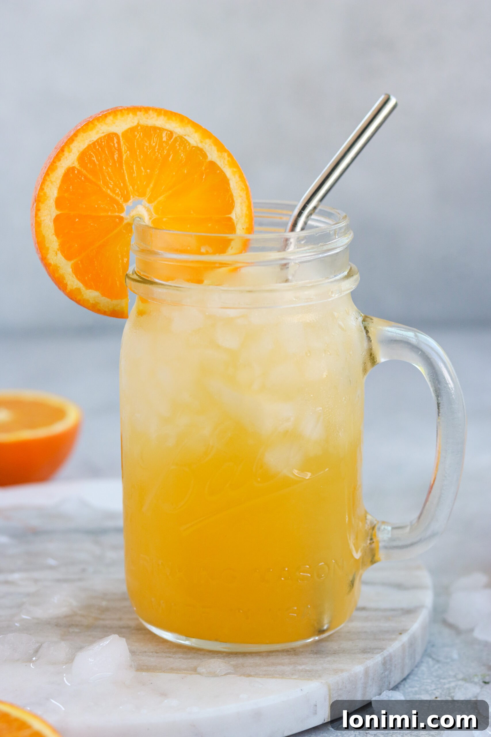 A close-up shot of a refreshing orange cocktail in a mason jar with a steel straw, surrounded by ice cubes and orange slices, highlighting its vibrant color.