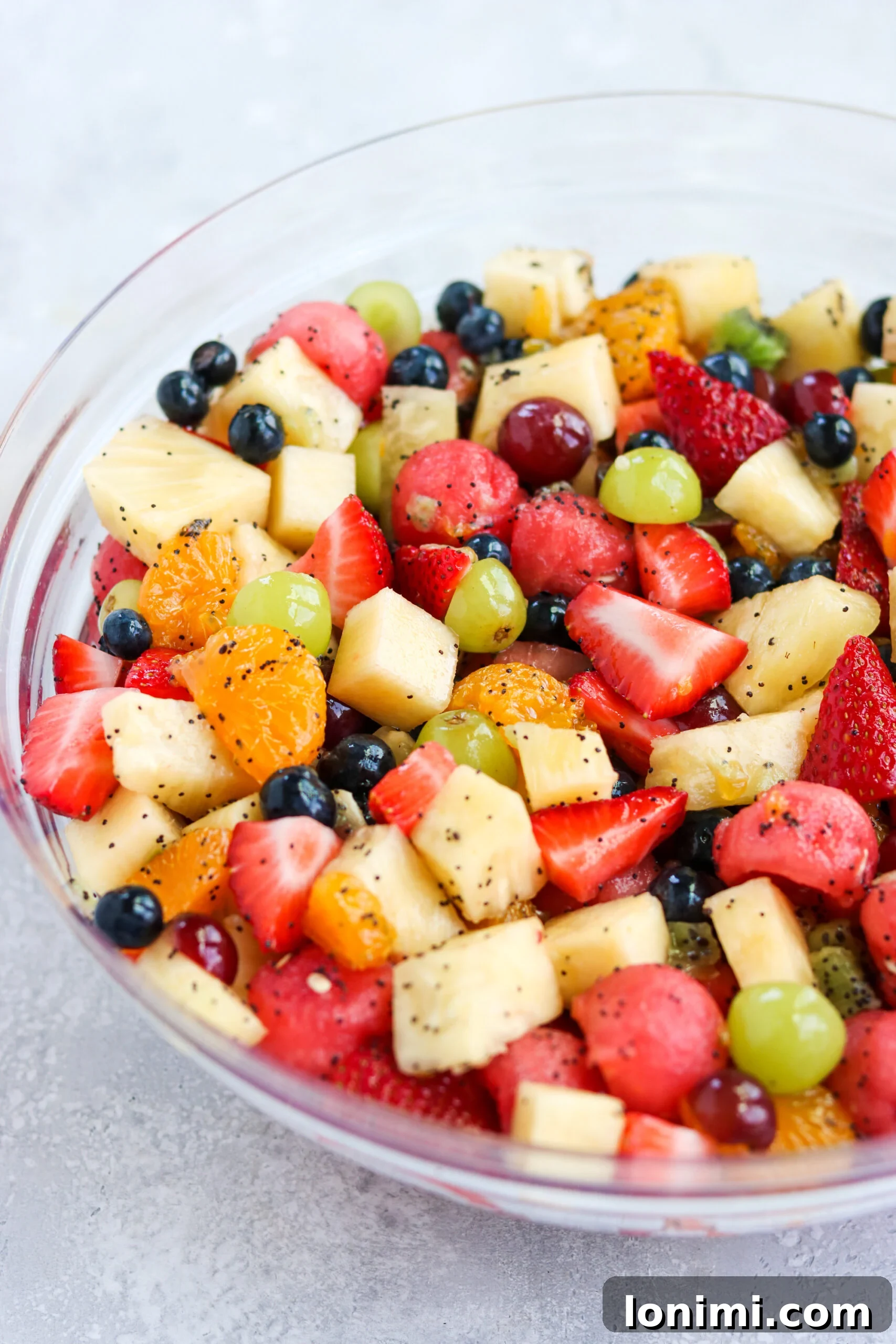 A large bowl of colorful Honey Lime Poppyseed Fruit Salad, showcasing a variety of fresh fruits mixed with a light dressing.