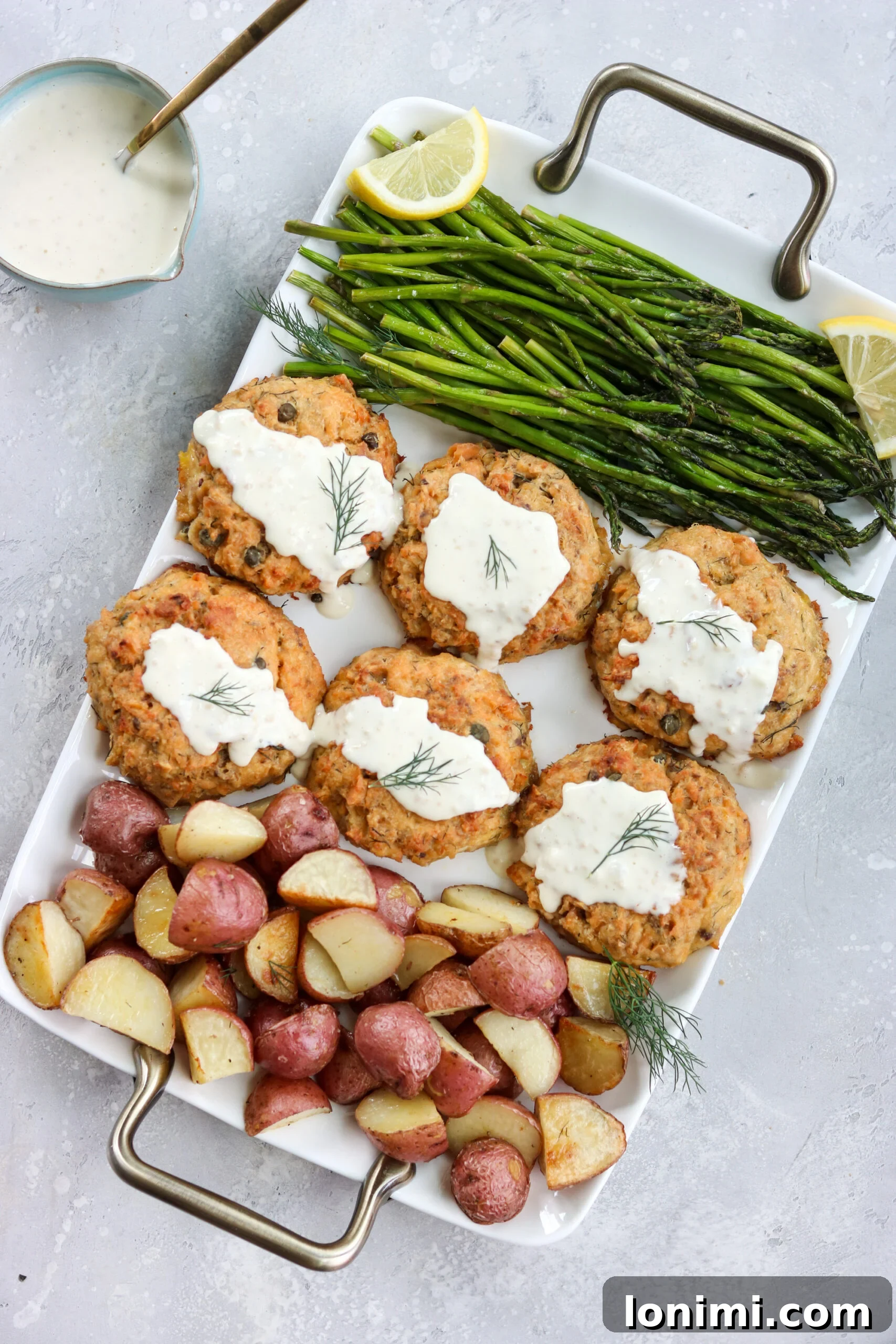 Healthy Sheet Pan Lemon Caper Salmon Patties 2 Tangy Lemon Caper Salmon Cakes with roasted asparagus and crispy potatoes on a sheet pan, ready to serve.