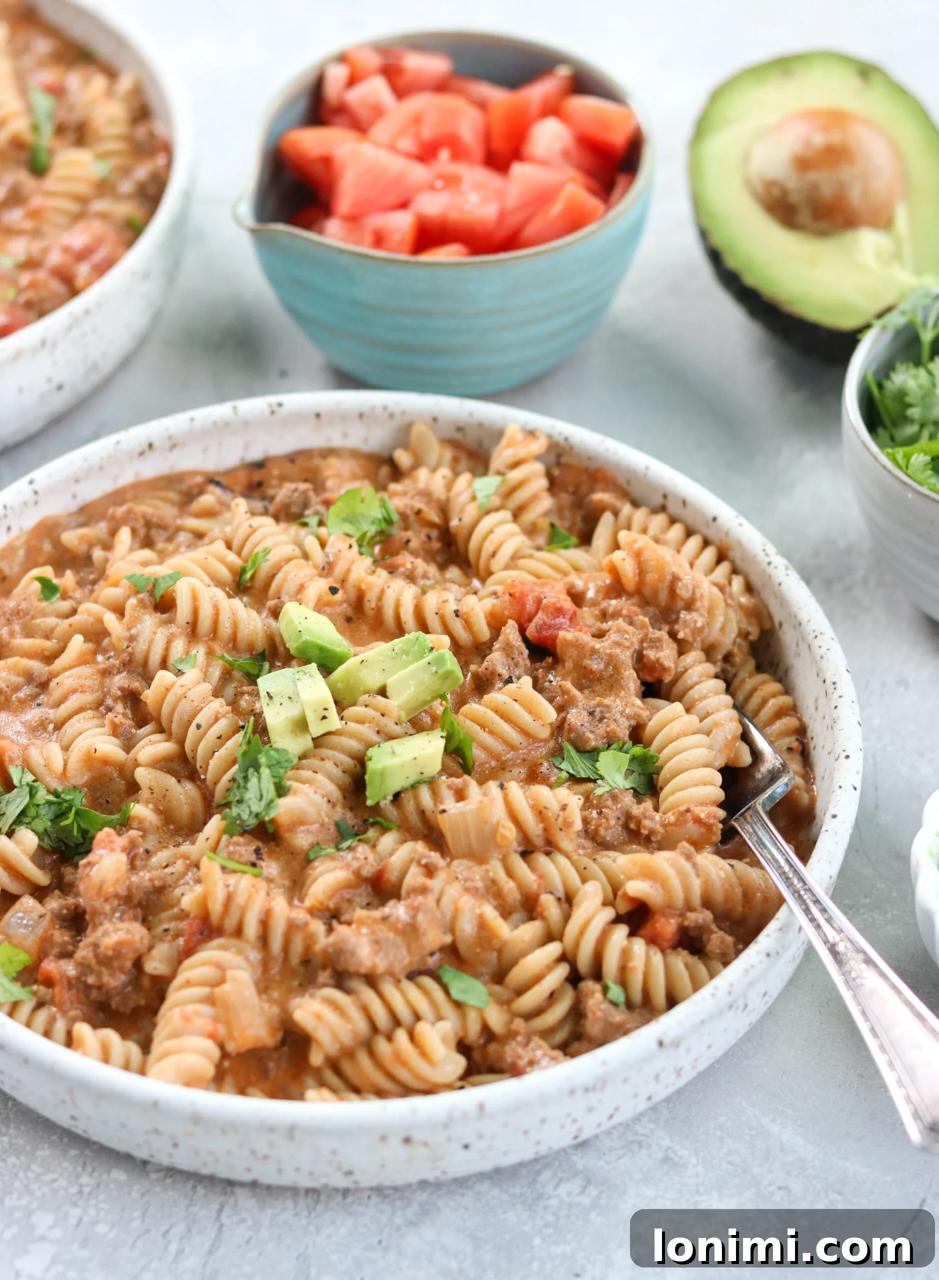 Instant Pot Taco Pasta served in a white bowl with a fork, garnished with fresh herbs