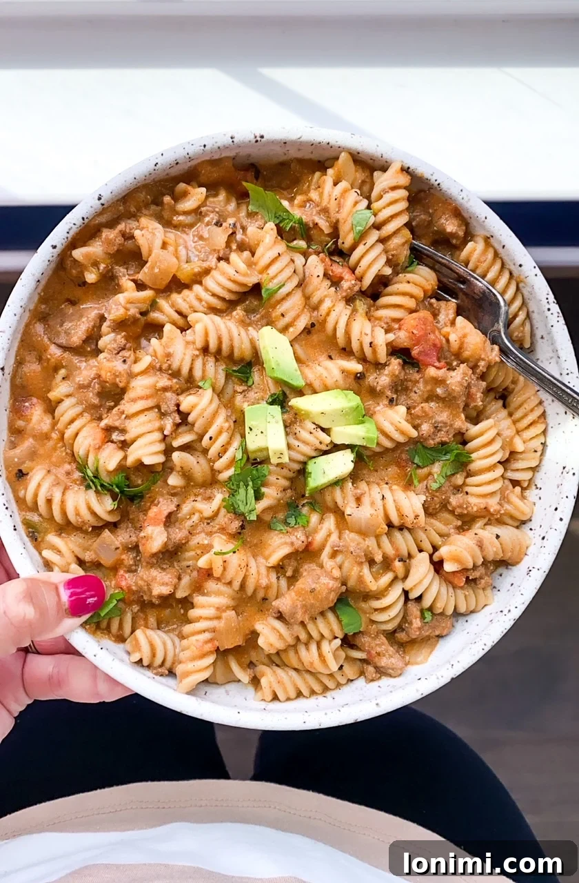 Person holding a white bowl filled with Instant Pot Taco Pasta, garnished with fresh toppings