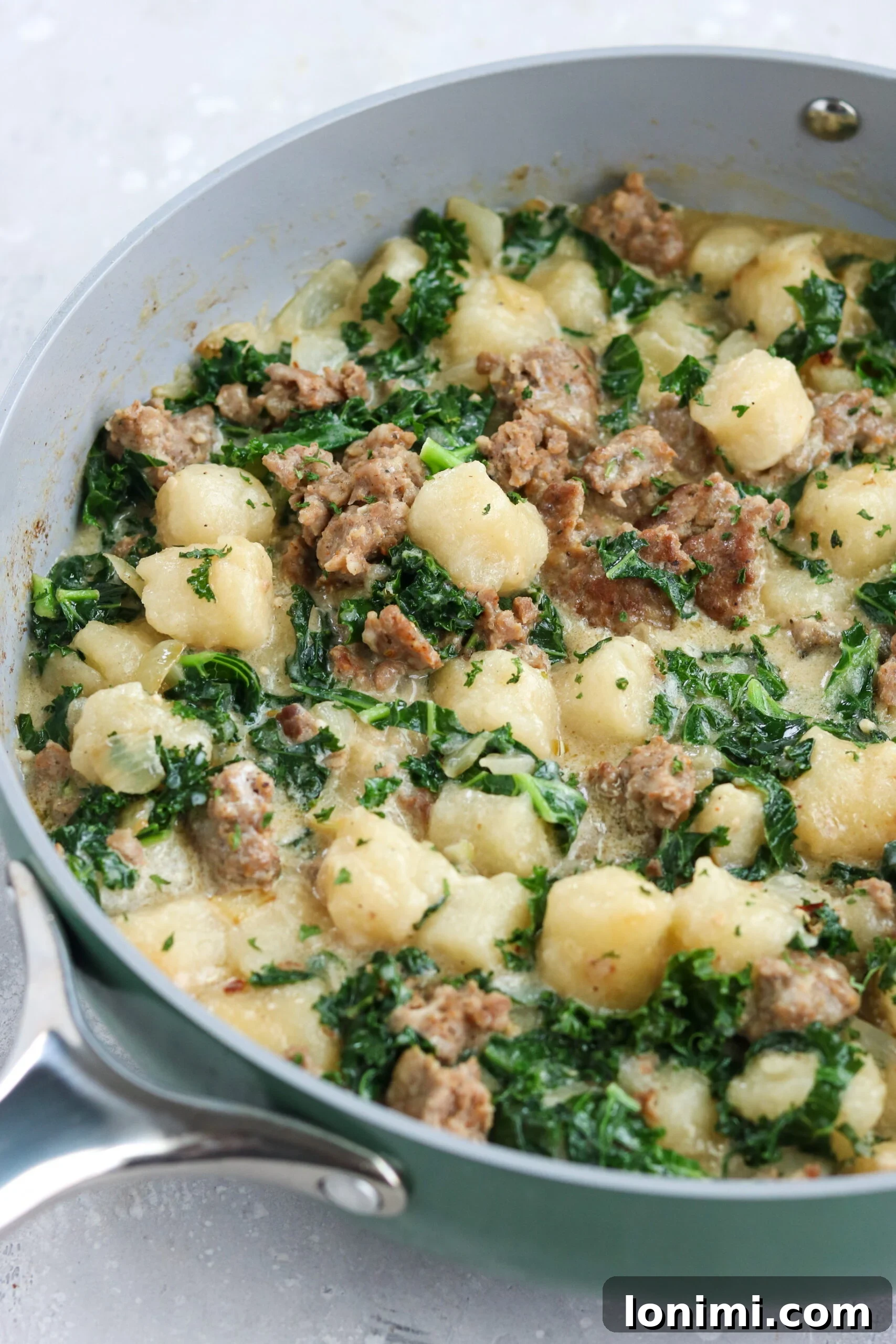 A large gray skillet filled with sizzling Paleo Sausage Kale Gnocchi, highlighting the vibrant colors and appealing texture of the cooked dish.