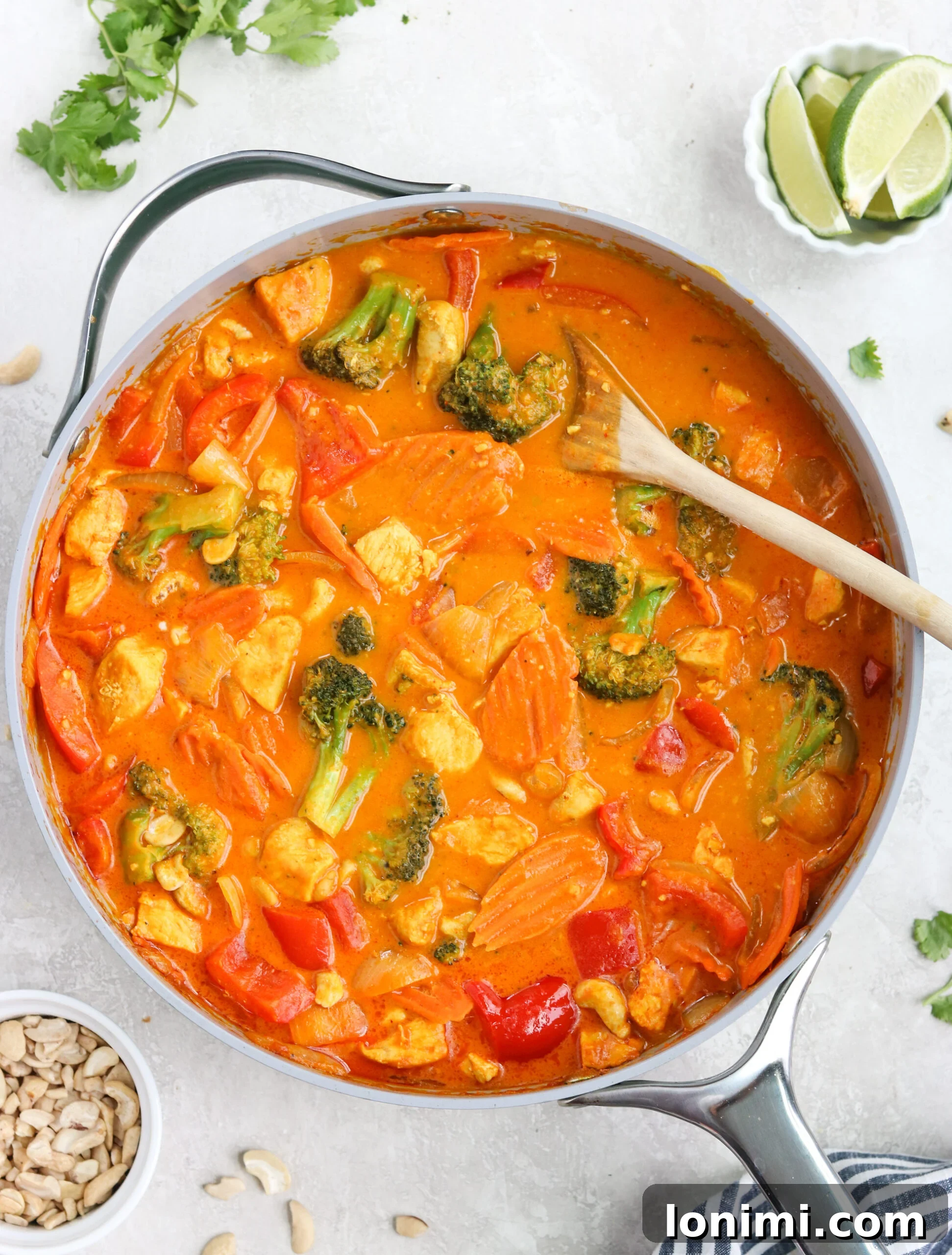 Paleo Pumpkin Curry Recipe Overhead view of a vibrant pumpkin chicken curry simmering in a gray skillet with a silver handle and a wooden spoon, set against a clean white background. This image highlights the rich texture of the Paleo Pumpkin Curry Recipe.