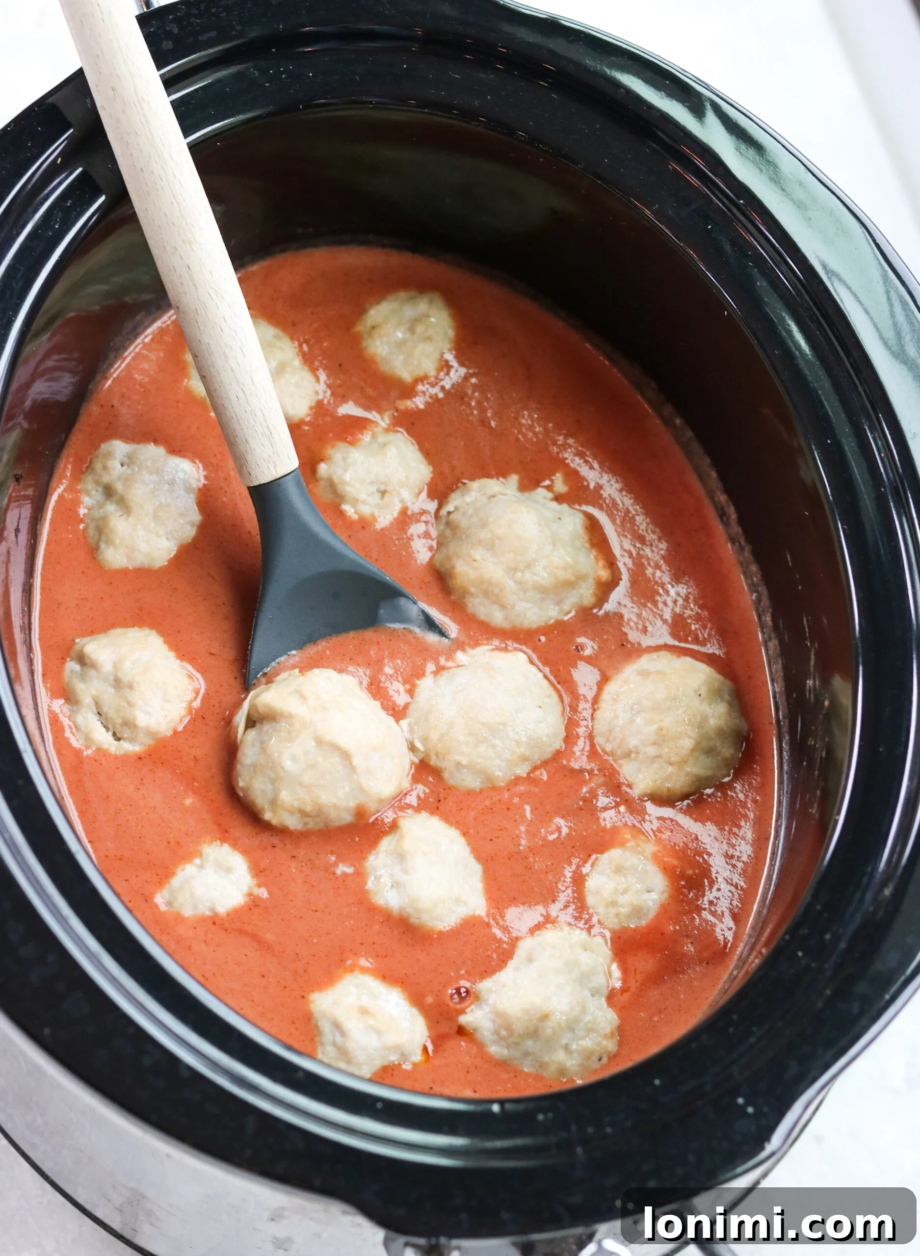 Baked Paleo Butter Chicken Bites 4 healthy chicken meatballs with creamy tomato curry sauce in a black slow cooker
