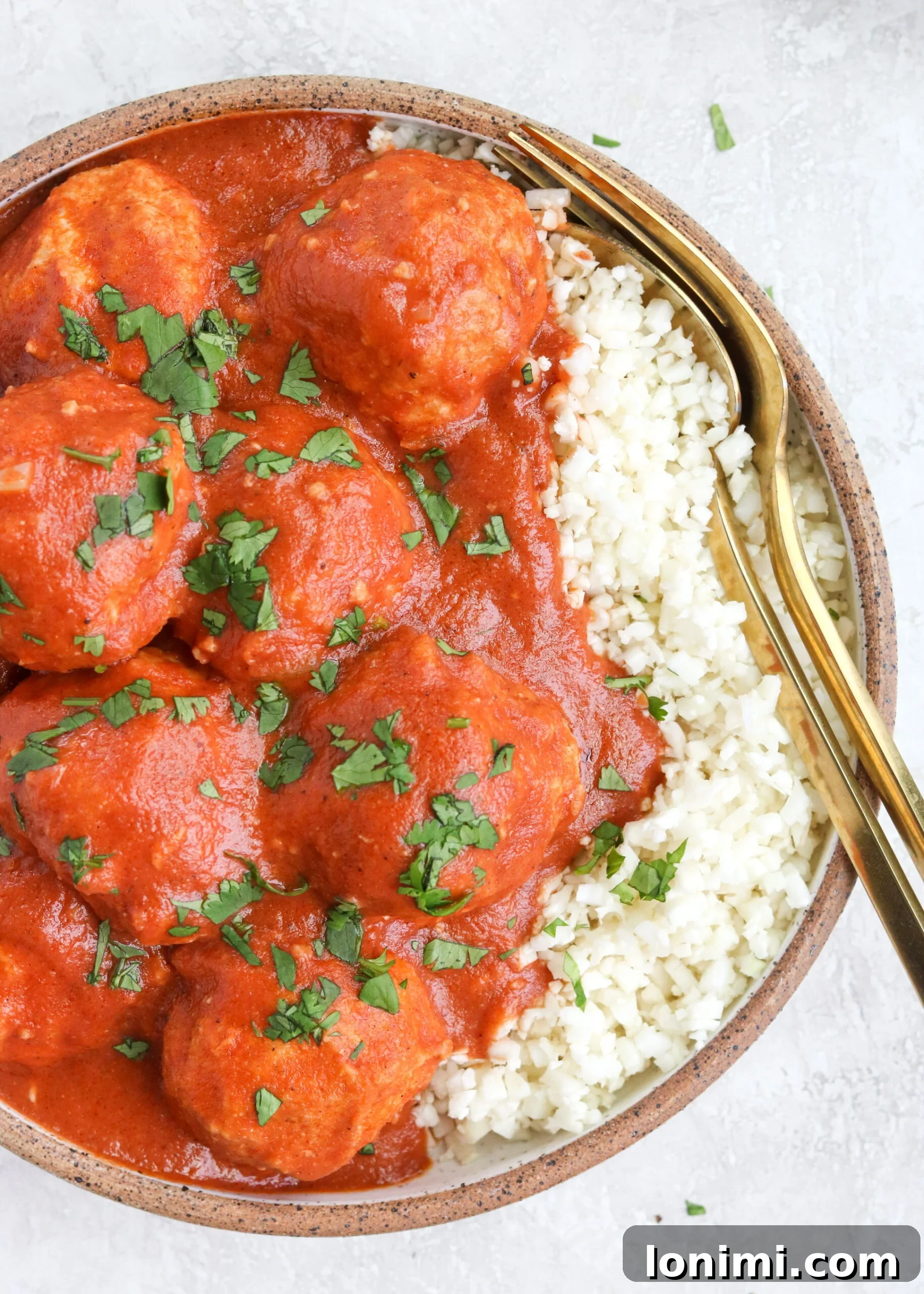 Baked Paleo Butter Chicken Bites 5 Creamy Garam Masala Curry Sauce with Ground Chicken Meatballs served over cauliflower rice in a bowl with two gold forks