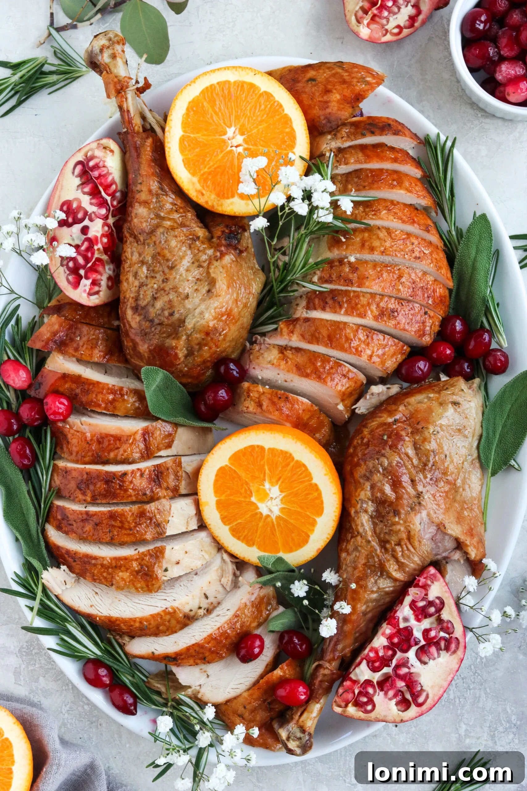 Paleo roasted turkey perfectly sliced and plated with two turkey legs, garnished with fresh herbs.