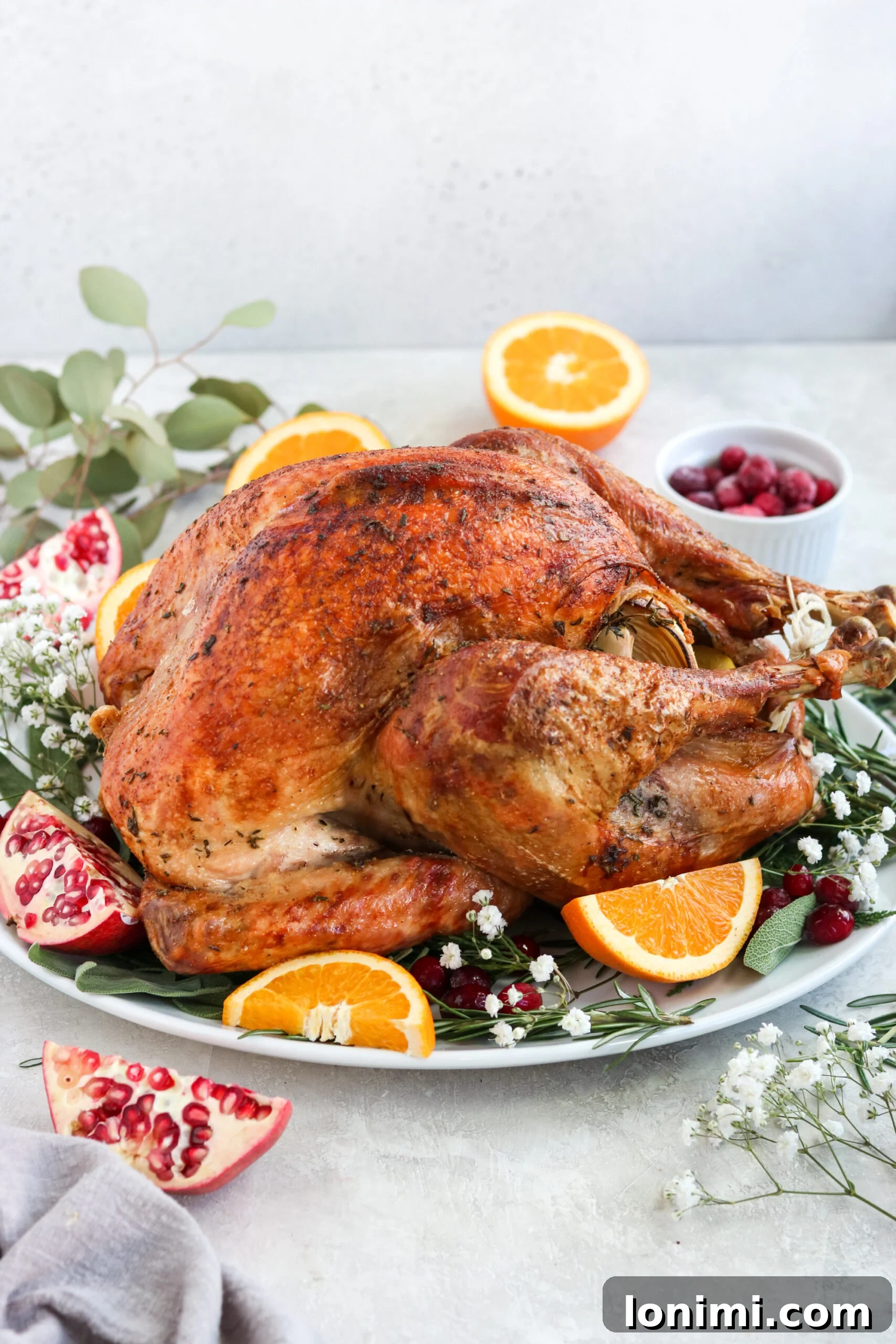 A beautifully roasted turkey on a white platter, garnished with fresh herbs and citrus, before carving.