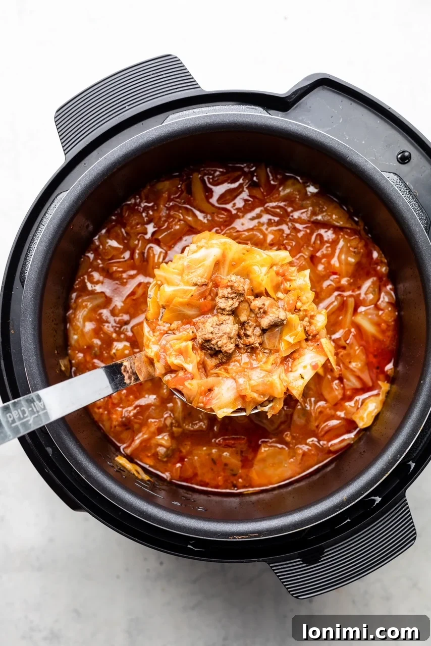 An Instant Pot filled with simmering unstuffed cabbage soup, ready to be served with a ladle resting inside.