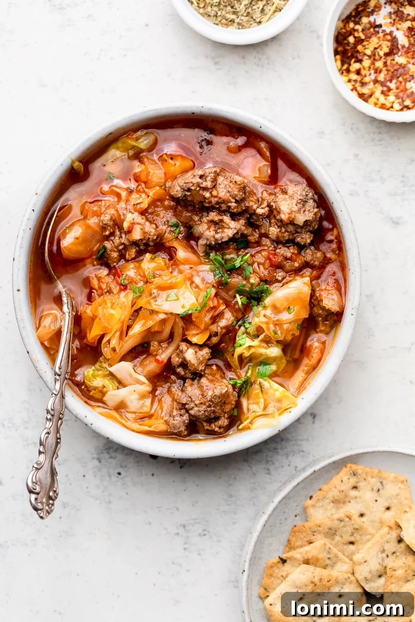 A steaming bowl of Instant Pot Unstuffed Cabbage Soup, garnished with fresh parsley, served with a silver spoon and a side of crackers, ready for a comforting meal.