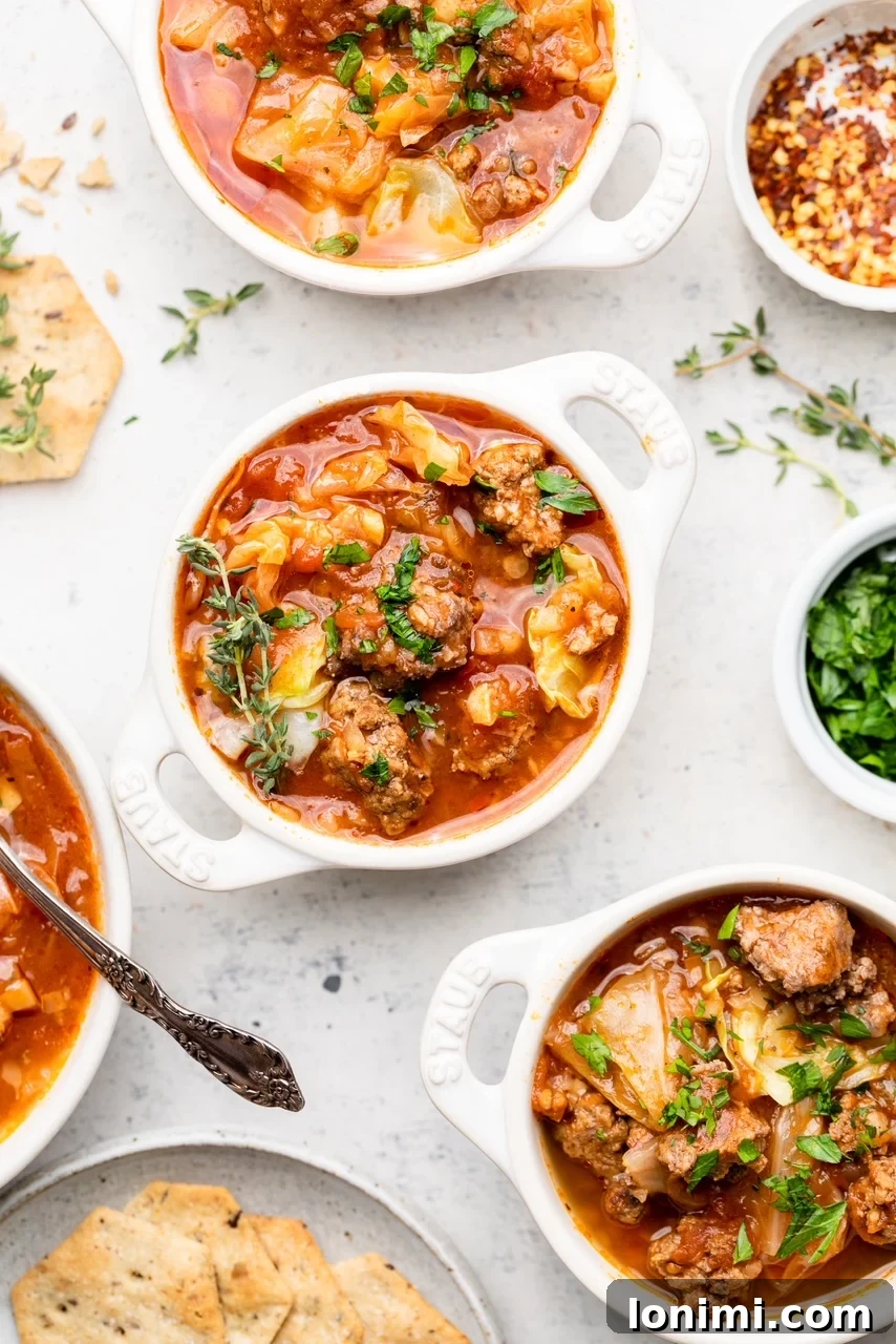 Three bowls of hearty unstuffed cabbage soup, garnished with fresh parsley and served with a small plate of crackers on the side.