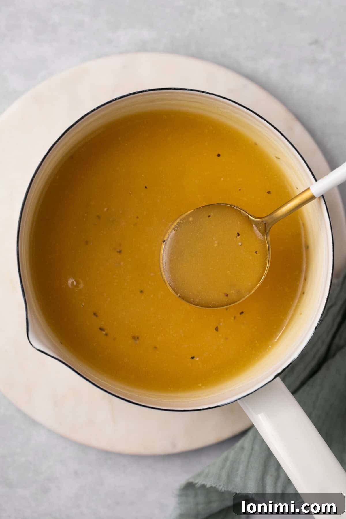 A close-up of luxurious, golden-brown gluten-free gravy resting in a charming sauceboat, accompanied by a silver spoon, ready to be served and enjoyed.