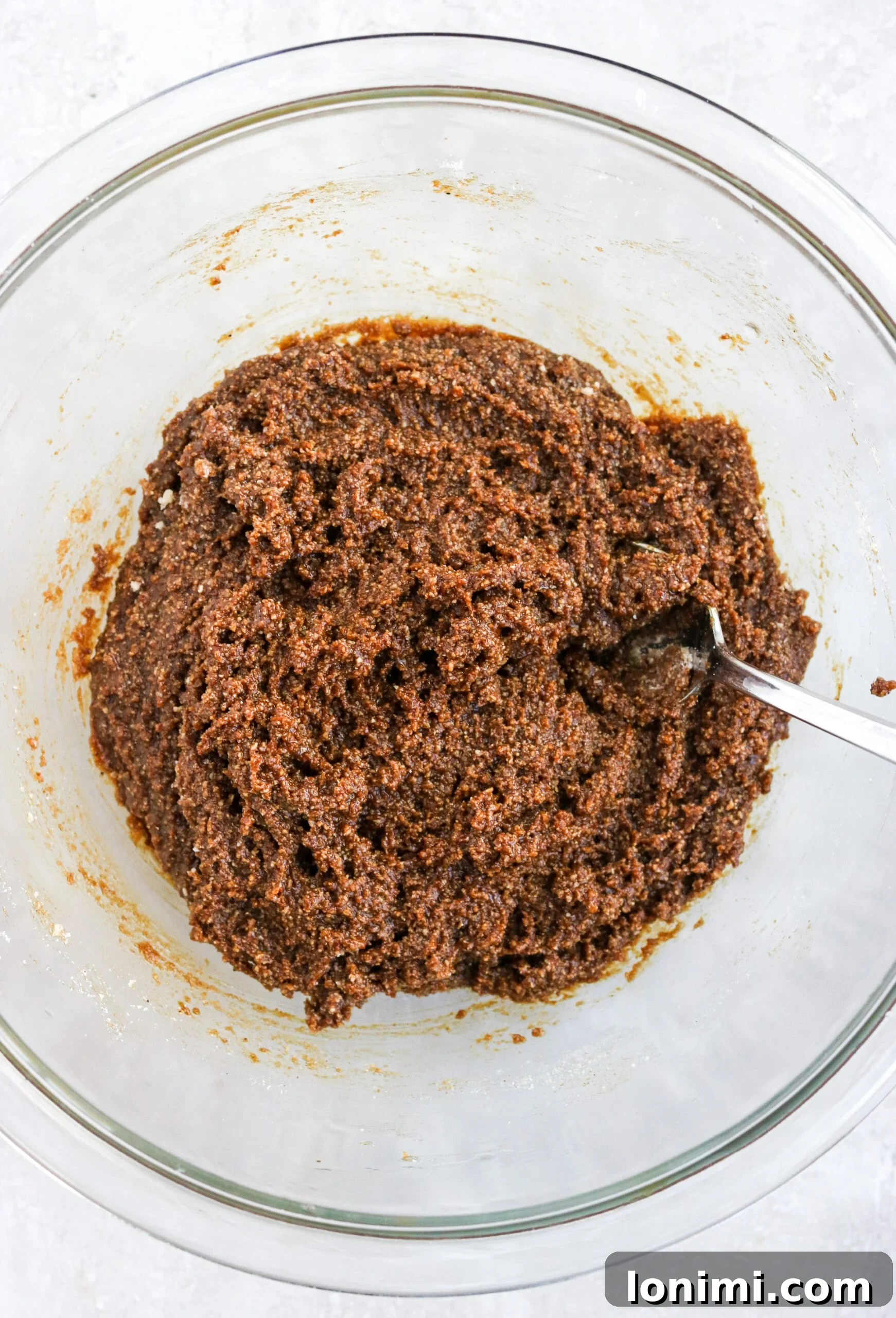 Effortless Gluten-Free Almond Flour Gingersnaps 4 gluten-free gingersnaps batter in a clear bowl with a spoon, showing its sticky texture.