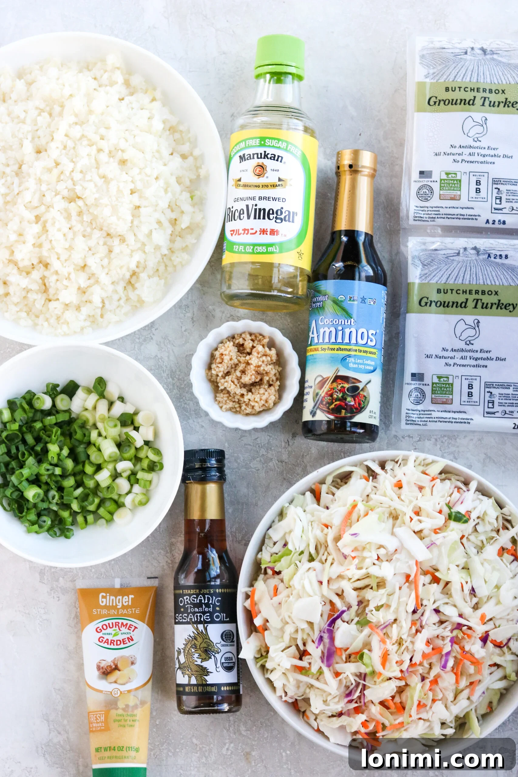 A flat lay photograph showcasing all the fresh and colorful ingredients laid out on a white surface, ready to be prepped for the healthy keto egg roll in a bowl, including ground turkey, fresh vegetables, and various sauces.