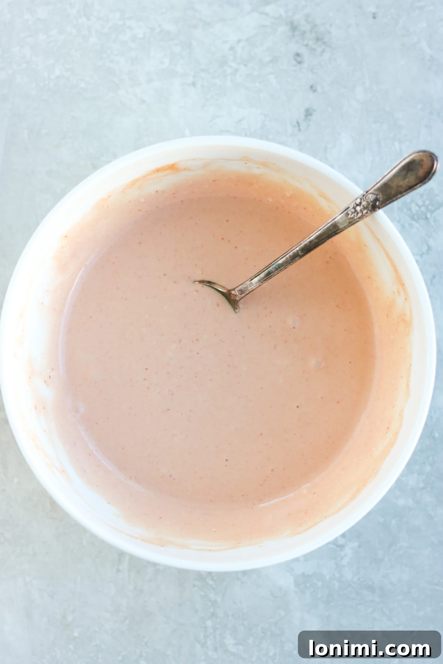 A close-up shot of the finished homemade spicy mayo, perfectly creamy and bright orange, served in a small white bowl with a elegant gold spoon, ready to be drizzled over your favorite dishes.
