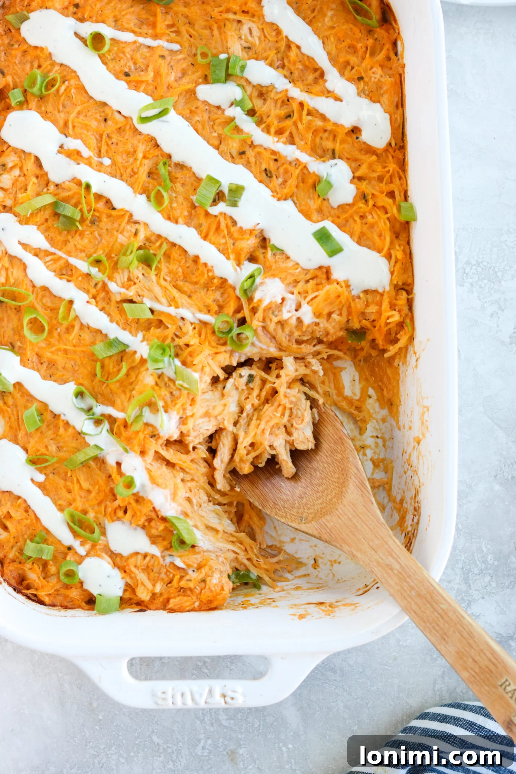 Guilt-Free Buffalo Chicken Spaghetti Squash Bake 2 Healthy Buffalo Chicken Spaghetti Squash Casserole, garnished with fresh herbs and a drizzle of ranch dressing, in a pristine white casserole dish, ready to be served.