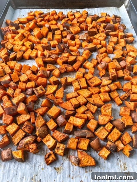 Perfectly cubed sweet potatoes seasoned and ready for roasting on parchment paper