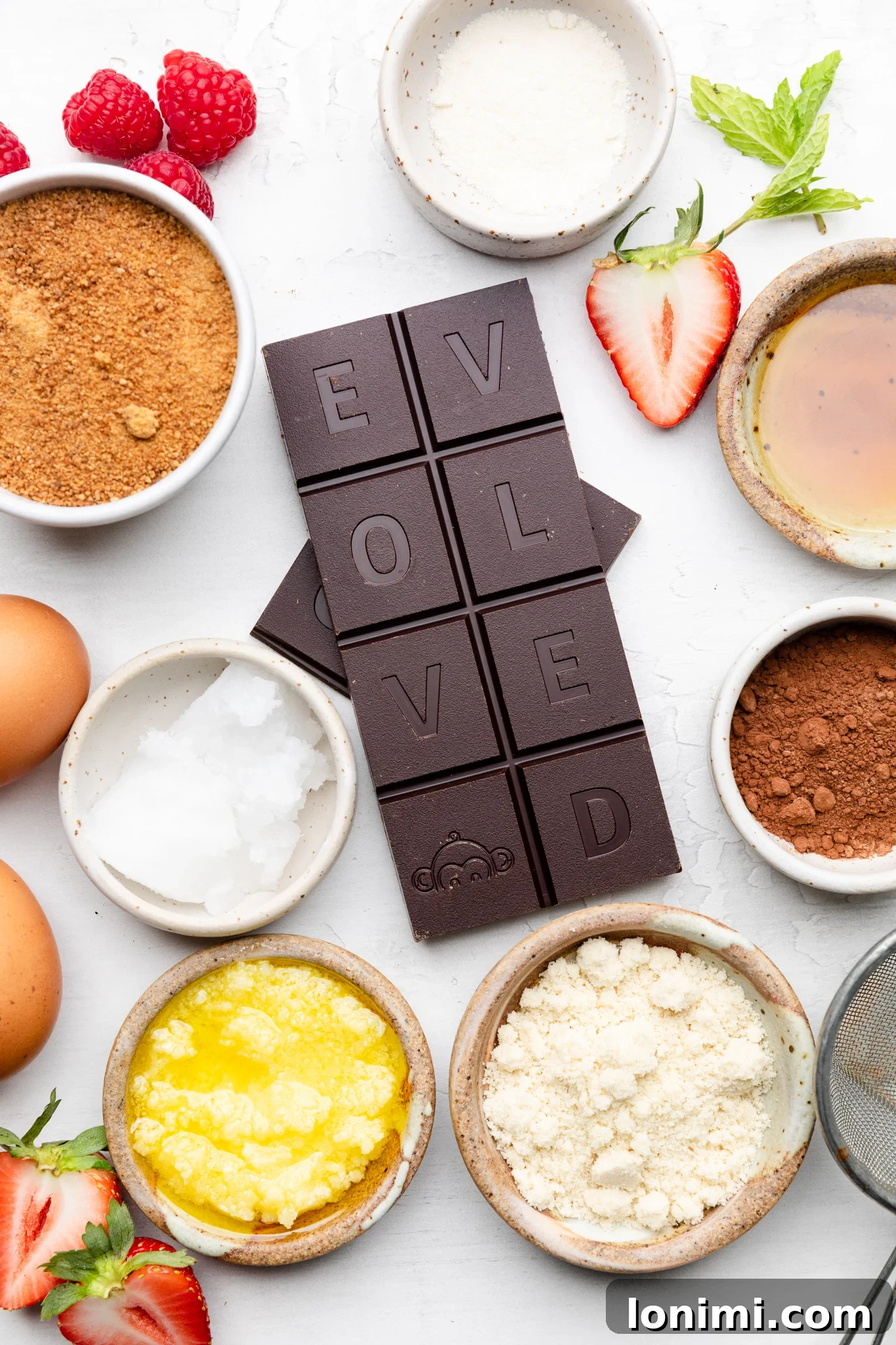 A flat lay image displaying all the ingredients for gluten-free mini chocolate lava cakes, including chunks of dark chocolate, coconut oil, ghee, eggs, coconut sugar, maple syrup, almond flour, coconut flour, and cacao powder, neatly arranged for preparation.