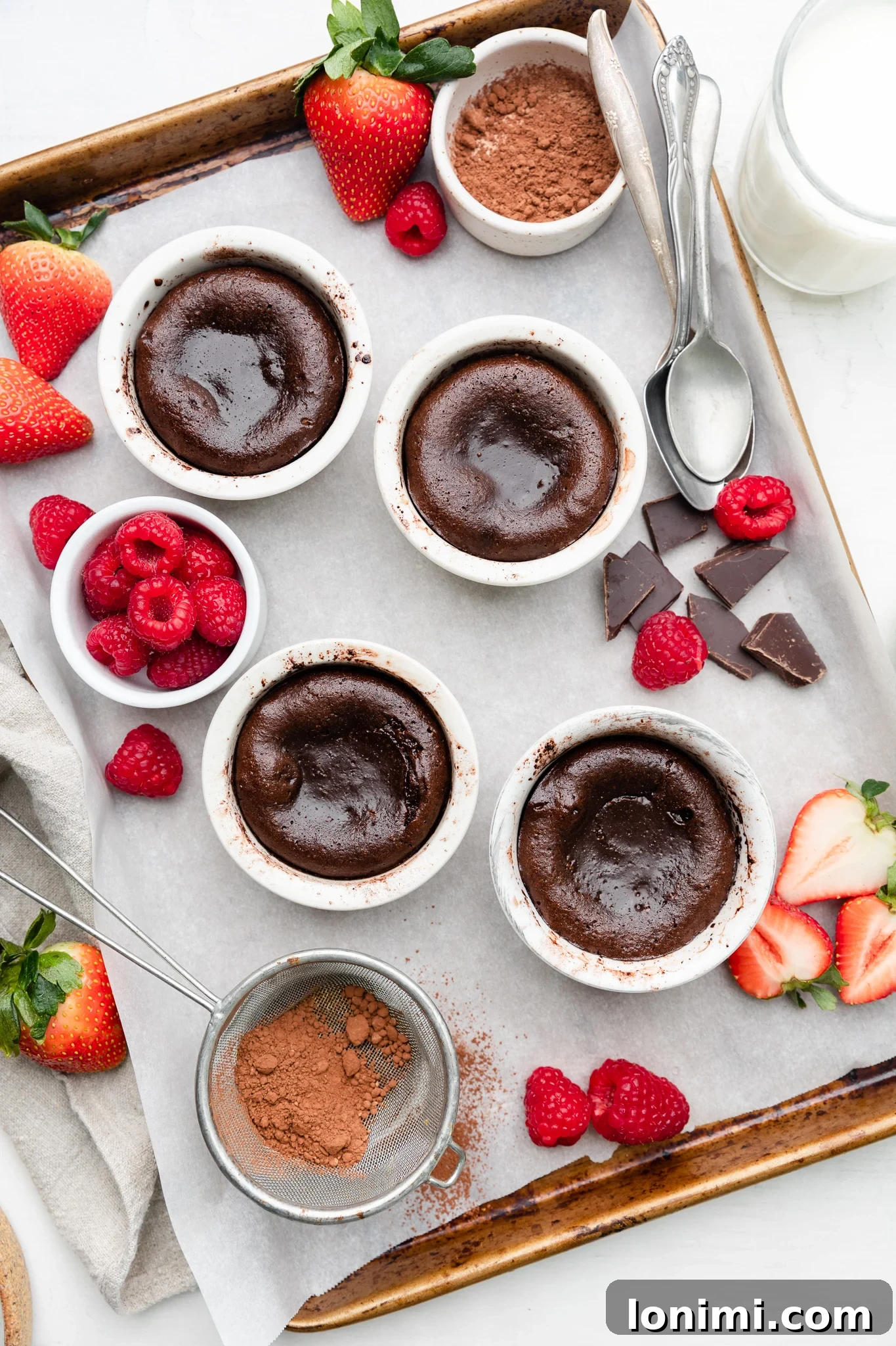 Gluten-free lava cakes arranged on a parchment-lined baking sheet, freshly out of the oven, with a scattering of mixed berries.
