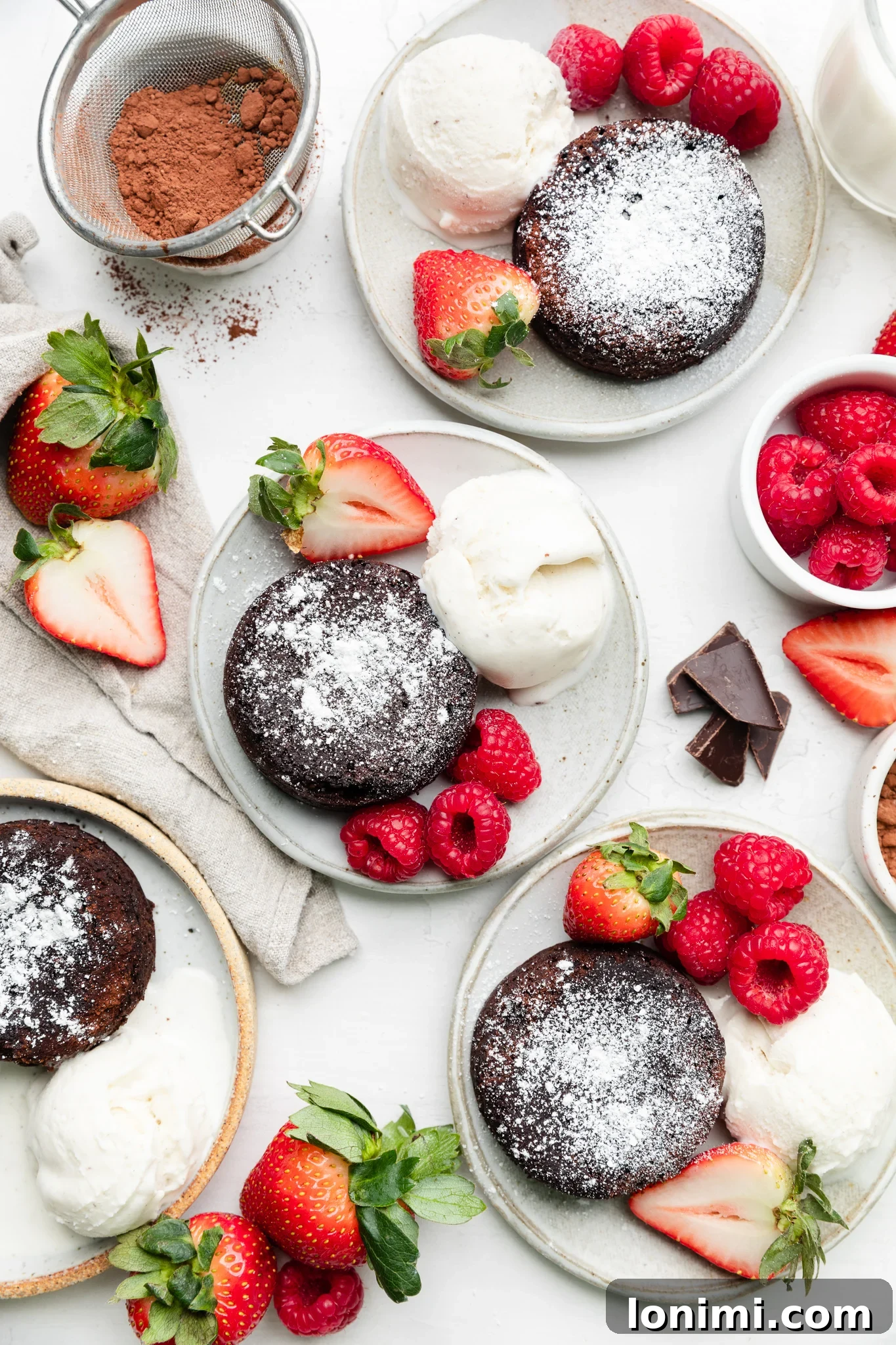 Four individual mini chocolate lava cakes presented on different plates, each garnished with a variety of fresh raspberries, strawberries, and scoops of vanilla ice cream, showcasing diverse and appealing serving options.