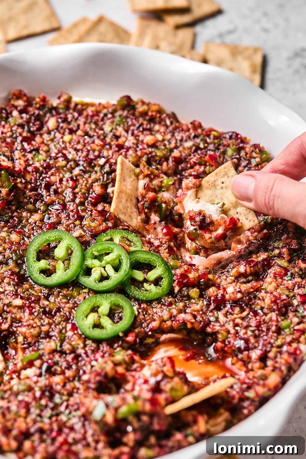 Dairy-Free Cranberry Jalapeno Dip: The Perfect Sweet Heat 11 a hand dipping a cracker into cranberry jalapeno dip