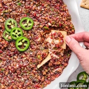 Dairy-Free Cranberry Jalapeno Dip: The Perfect Sweet Heat 13 cranberry jalapeno cream cheese dip in a white pie dish with a hand dipping a cracker in