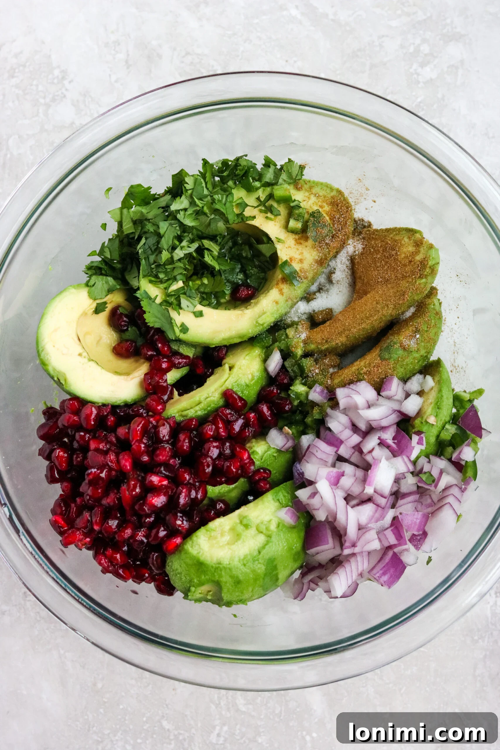 Ingredients for easy pomegranate guacamole laid out in a glass bowl
