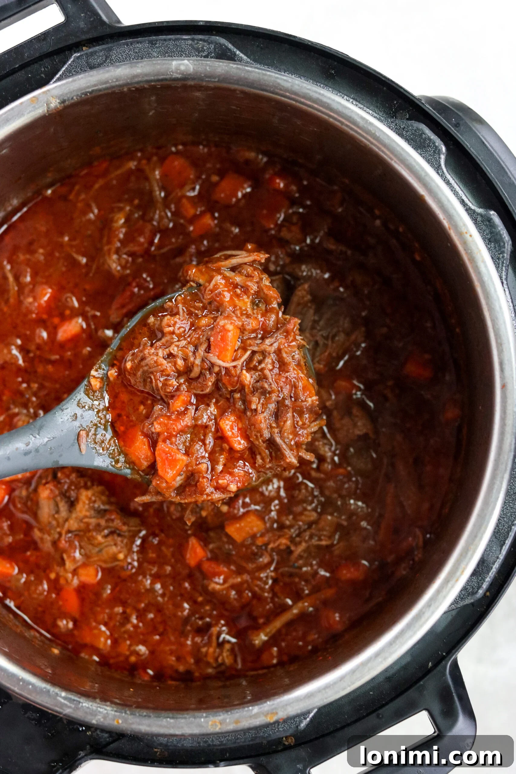 Finished short rib ragu simmering in the Instant Pot, with a serving spoon resting in the rich sauce.