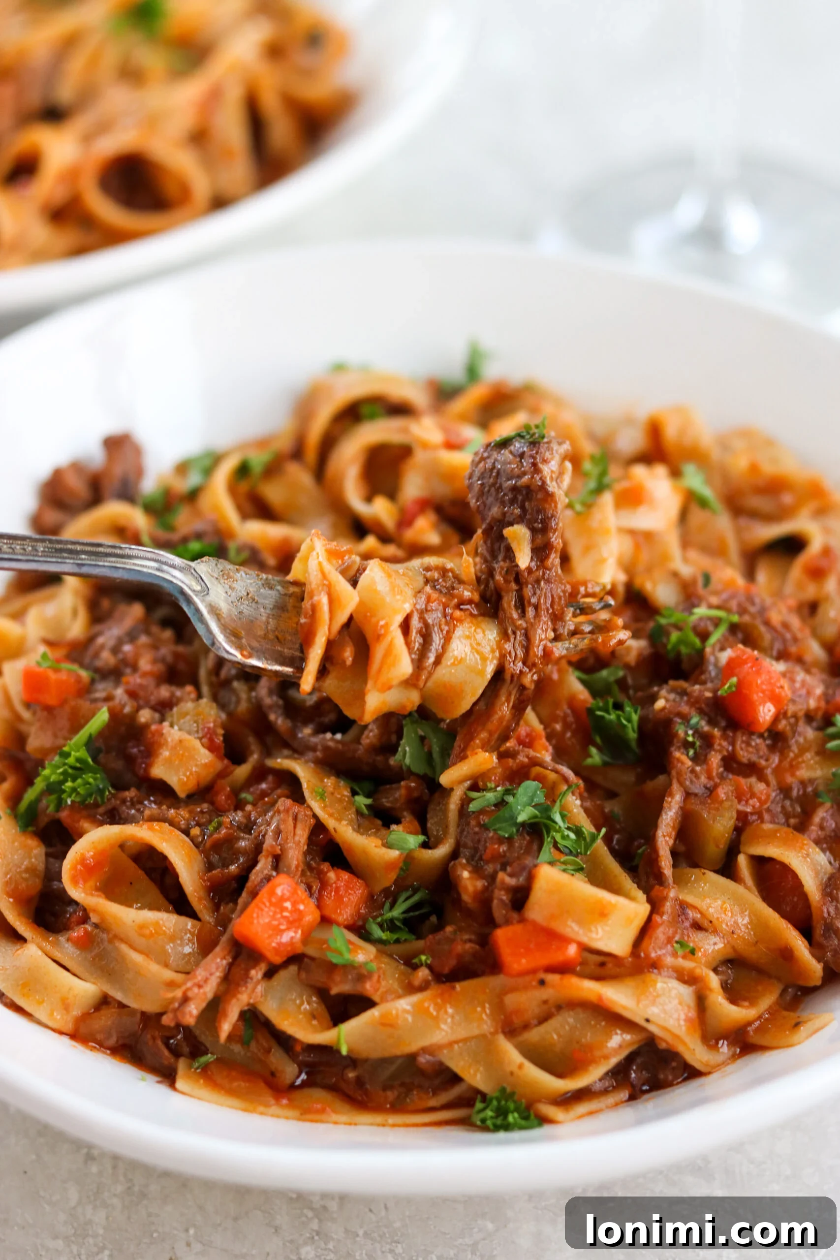 A forkful of tender beef short rib ragu in a white bowl, garnished with fresh parsley.
