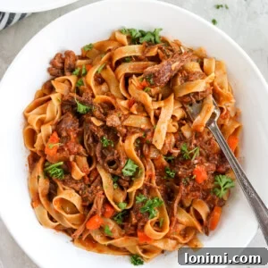 Instant Pot Short Rib Ragu in a white bowl with a fork and parsley