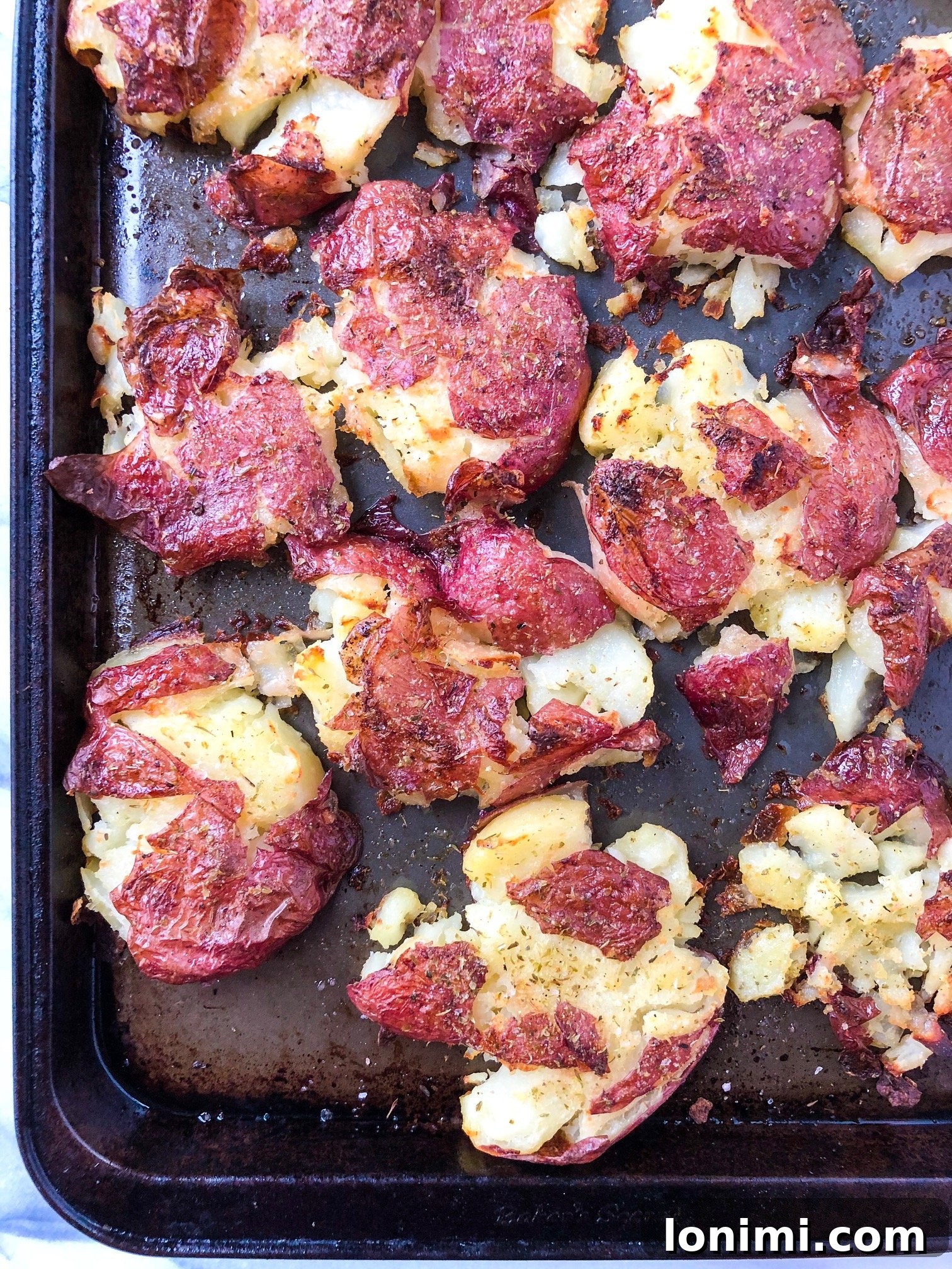 Golden-Crisp Smashed Potatoes with Fragrant Herb Ghee 2 Close-up of golden, crispy smashed potatoes garnished with fresh herbs.