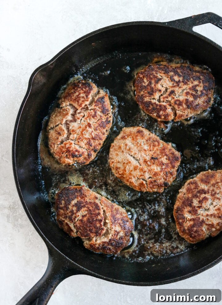 Grandma's Comfort Salisbury Steak with Savory Mushroom Gravy 5 Hamburger steaks sizzling and frying in a cast iron skillet