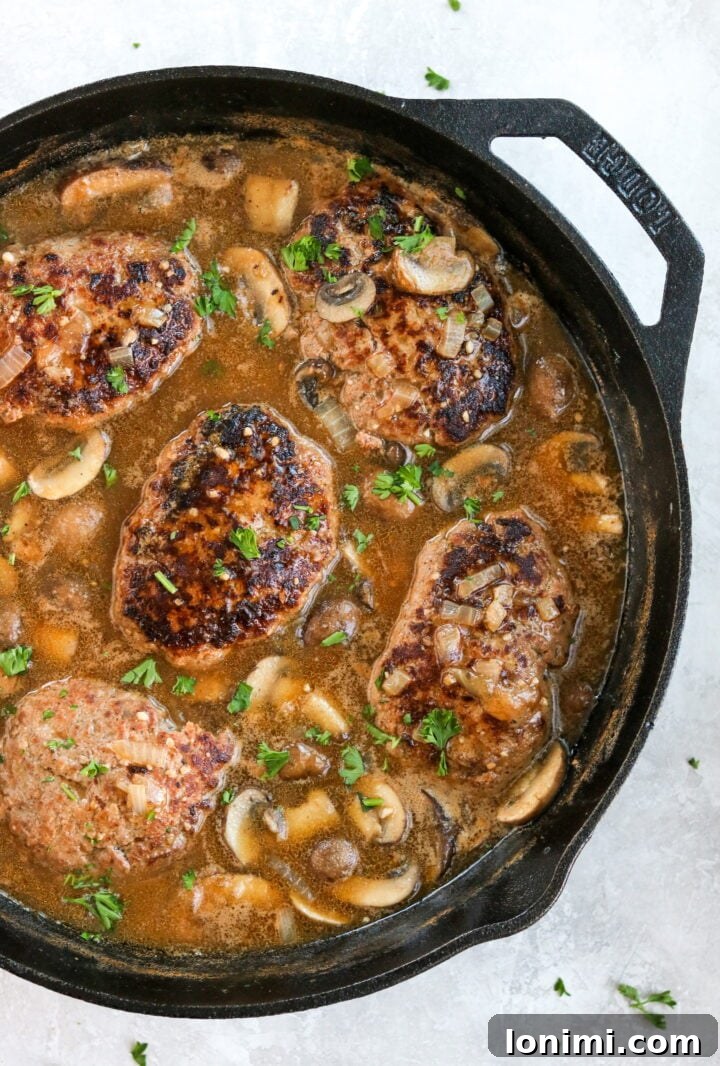 Grandma's Comfort Salisbury Steak with Savory Mushroom Gravy 7 Salisbury steak patties submerged in rich mushroom gravy in a cast iron pan, ready to serve